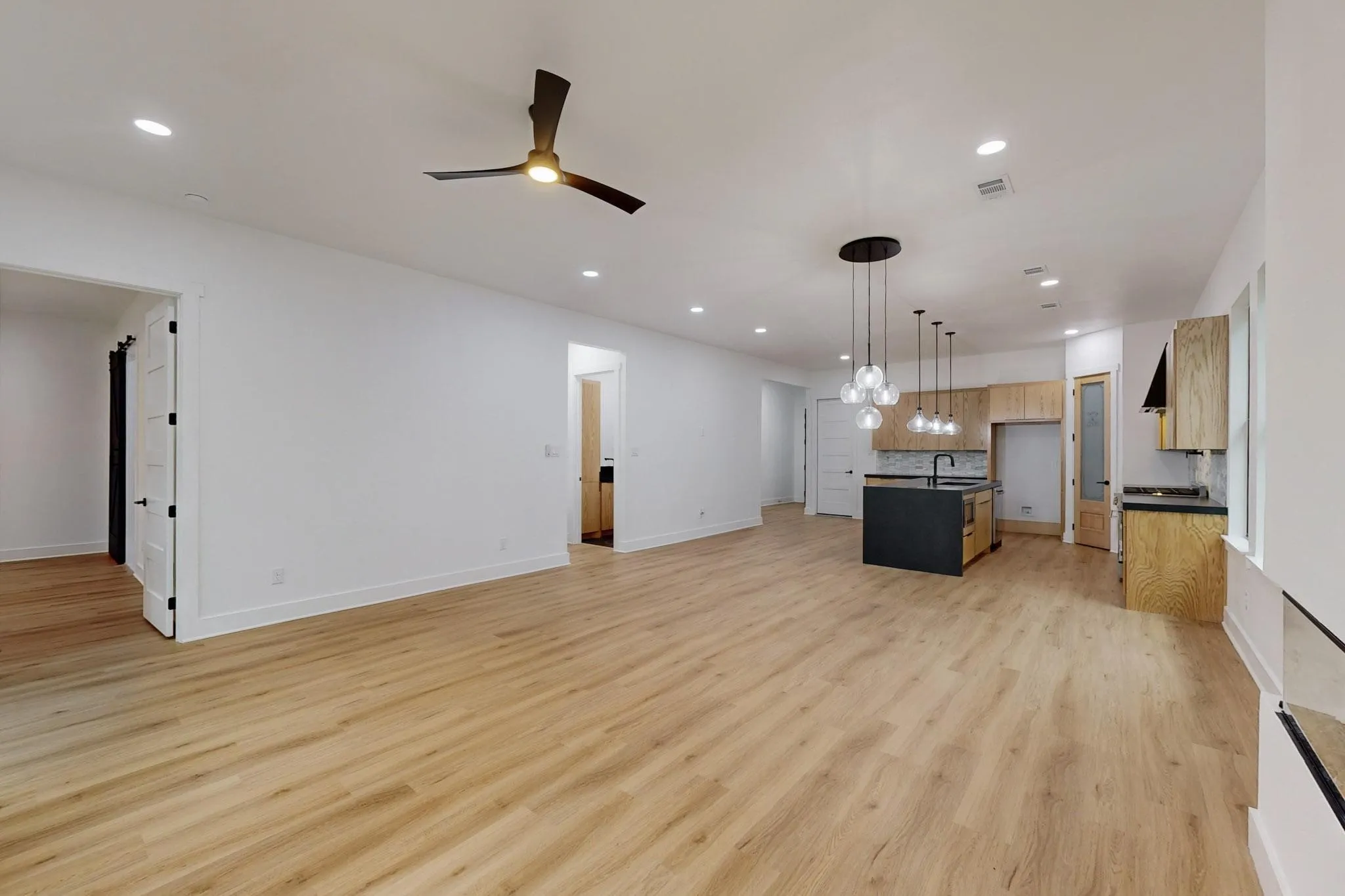 Expansive open-concept living area featuring light wood-finish flooring, recessed lighting, and a contemporary ceiling fan