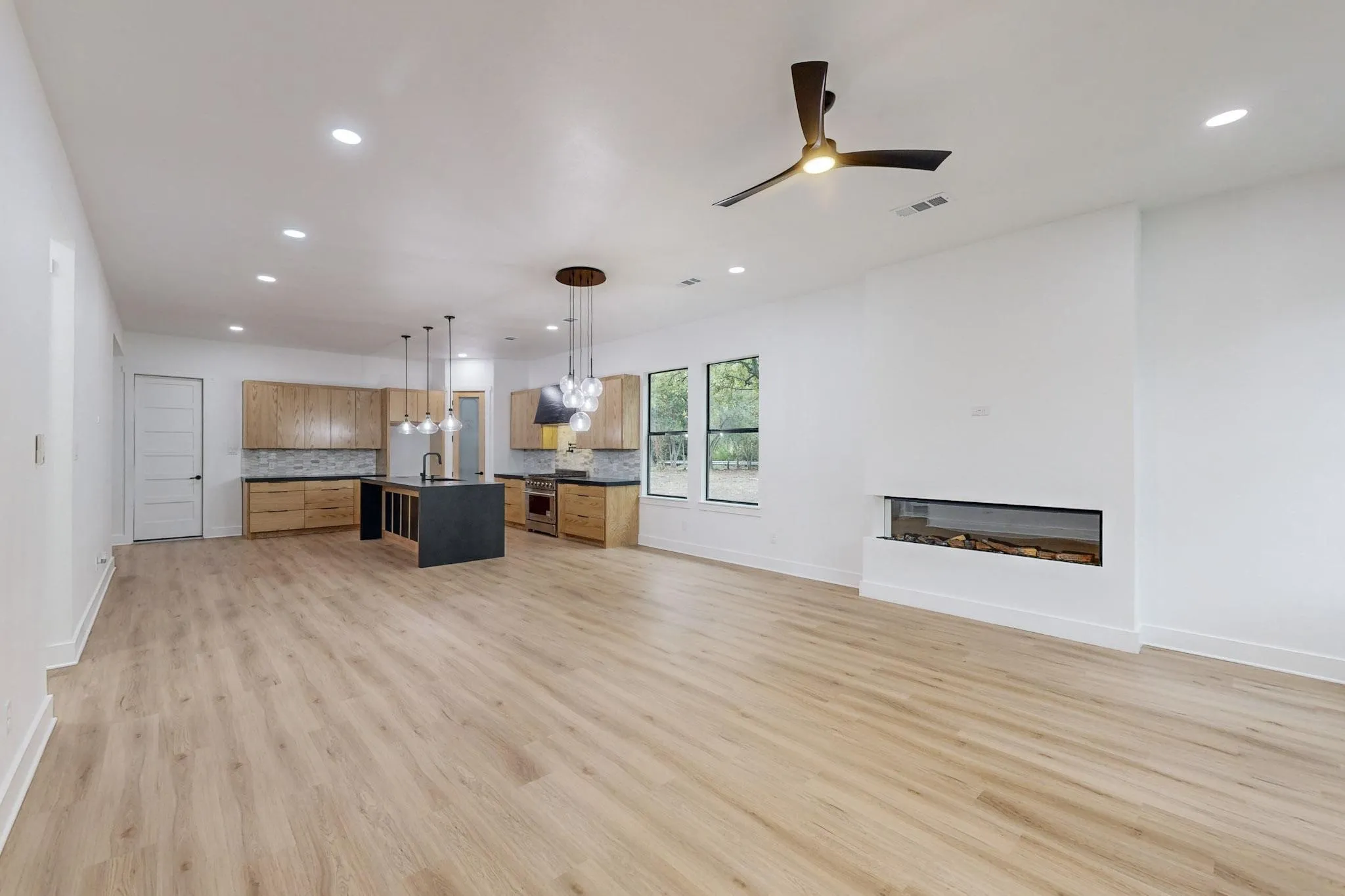 Spacious open-concept living area featuring wood-finish flooring, recessed lighting, and a modern linear fireplace
