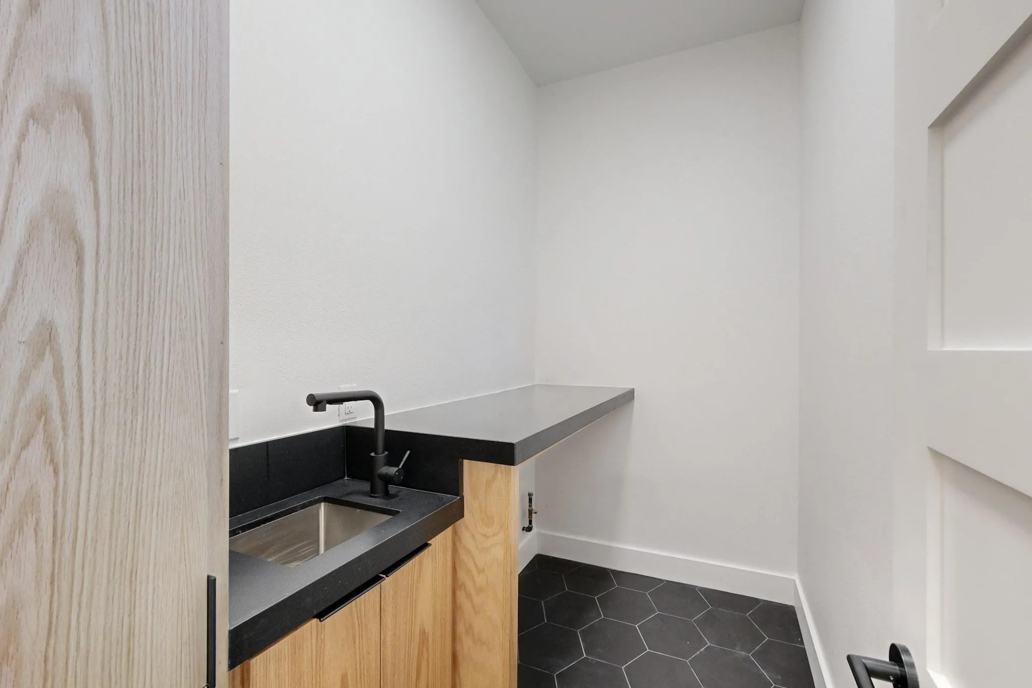 Utility space featuring a wood-finish cabinet, black countertop with integrated sink, matte black faucet, and hexagonal floor tiles