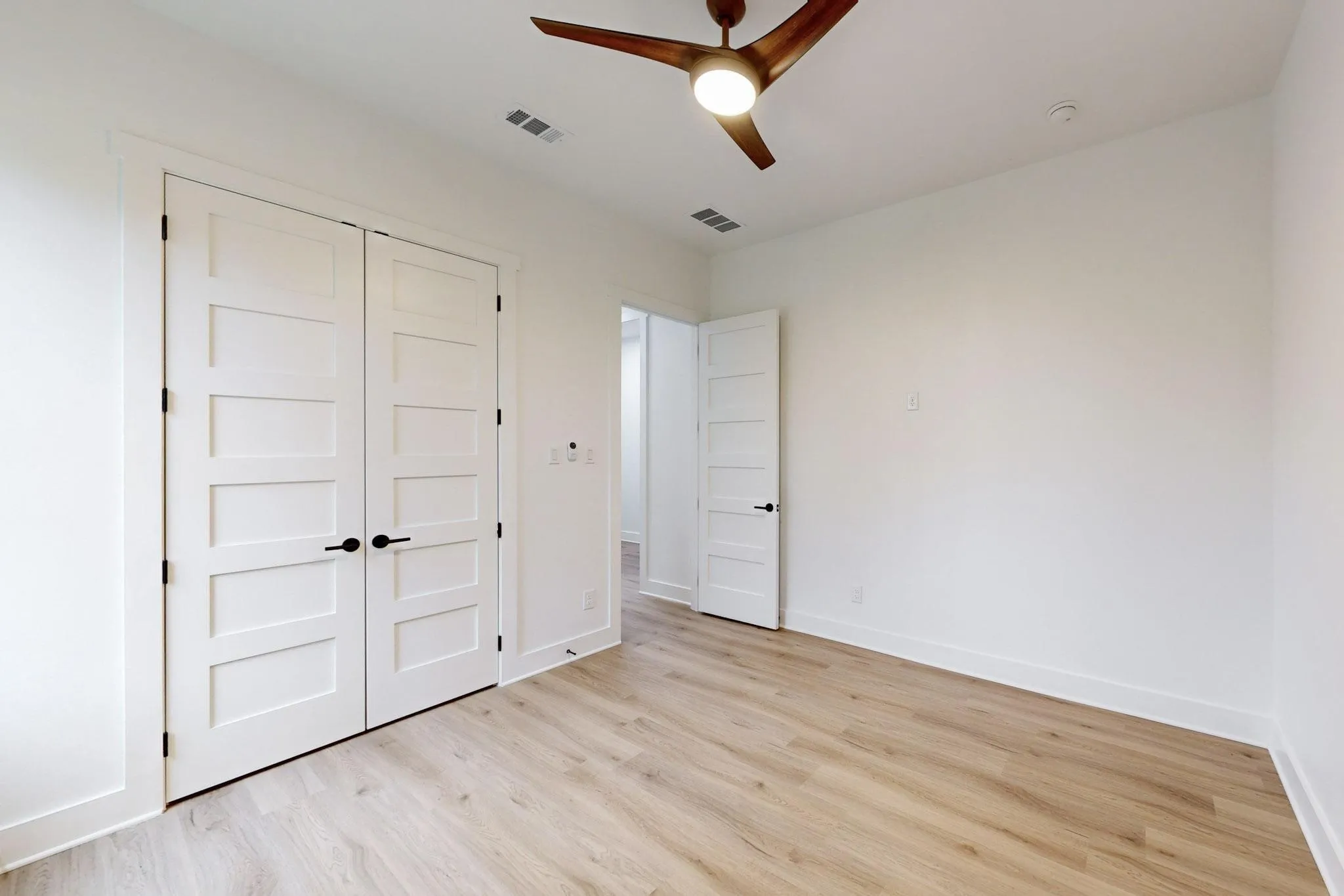 Spacious room featuring wood-finish flooring, crisp white walls, and a contemporary ceiling fan with integrated lighting