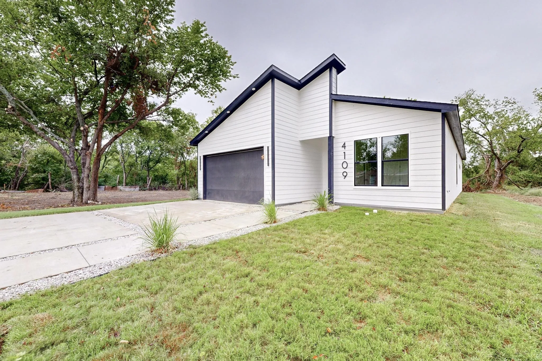 Contemporary exterior featuring white siding with dark trim accents, a dark garage door, and a concrete driveway