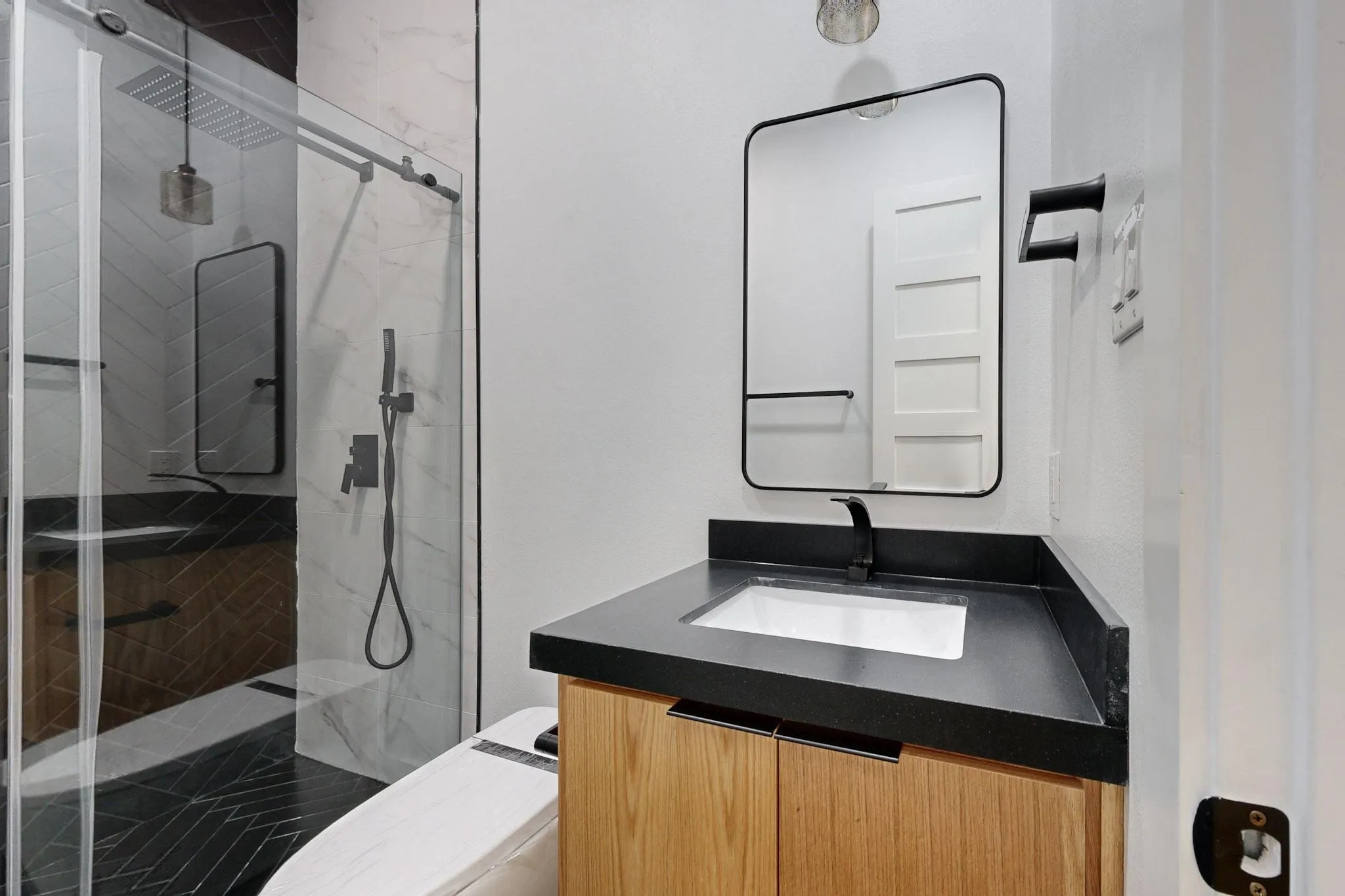 Modern bathroom featuring a wood-finish vanity with a black countertop, a rectangular undermount sink, and a black-framed mirror