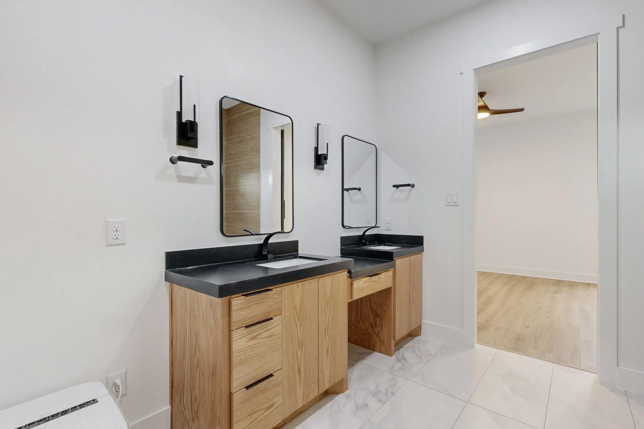 Double vanity featuring wood-finish cabinetry, dark countertops, and matte black fixtures