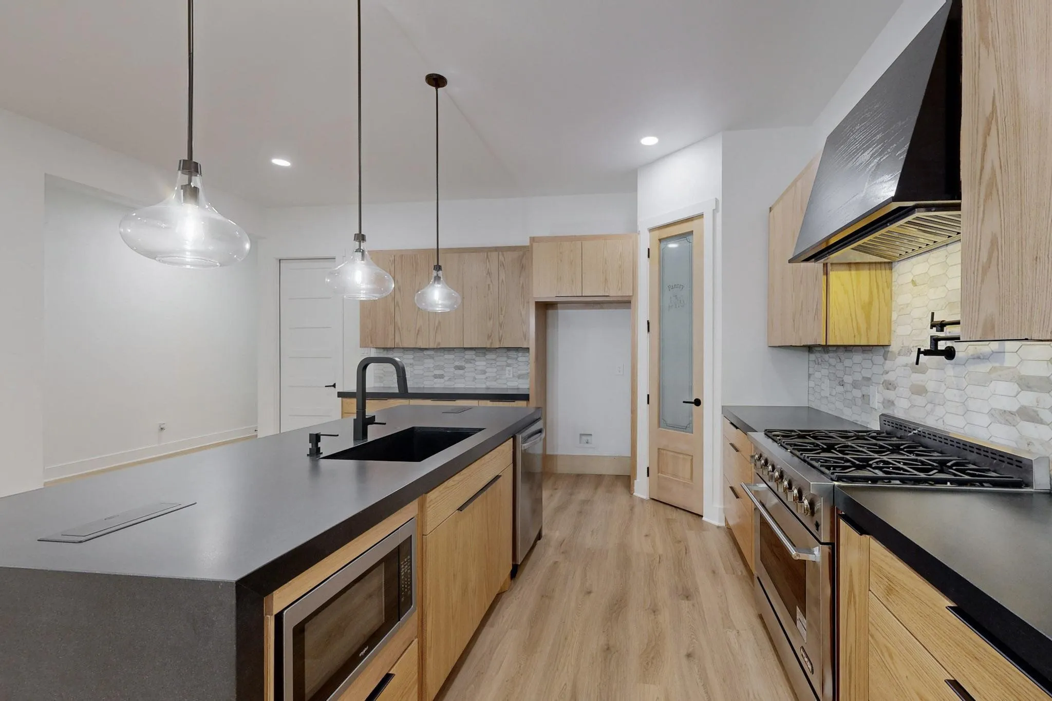 Contemporary kitchen featuring light wood-finish cabinetry, dark countertops, and wood-finish flooring