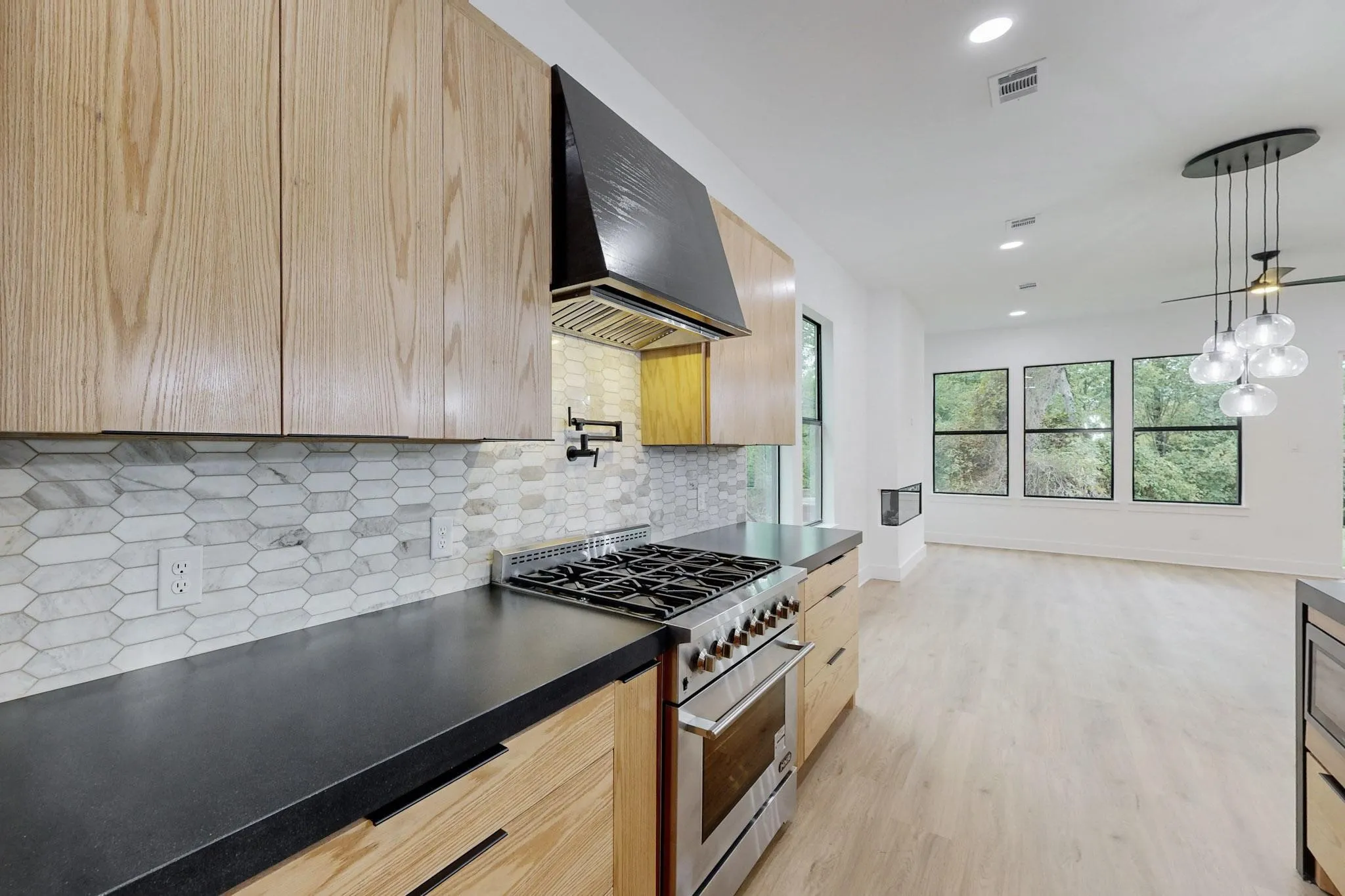 Modern kitchen featuring light wood-finish cabinetry, dark countertops, and a white hexagon tile backsplash