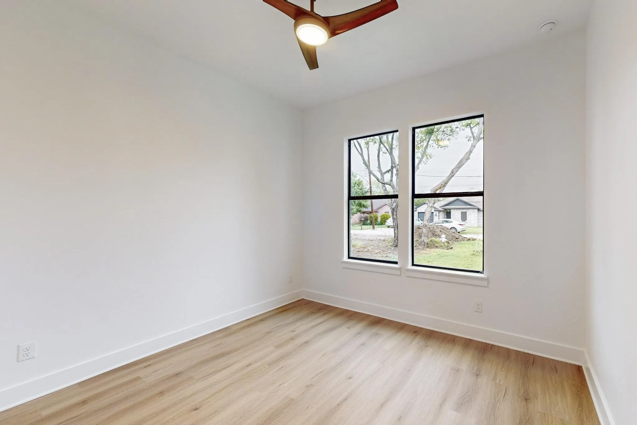 Room featuring wood-finish flooring, crisp white walls, and a contemporary ceiling fan with integrated lighting
