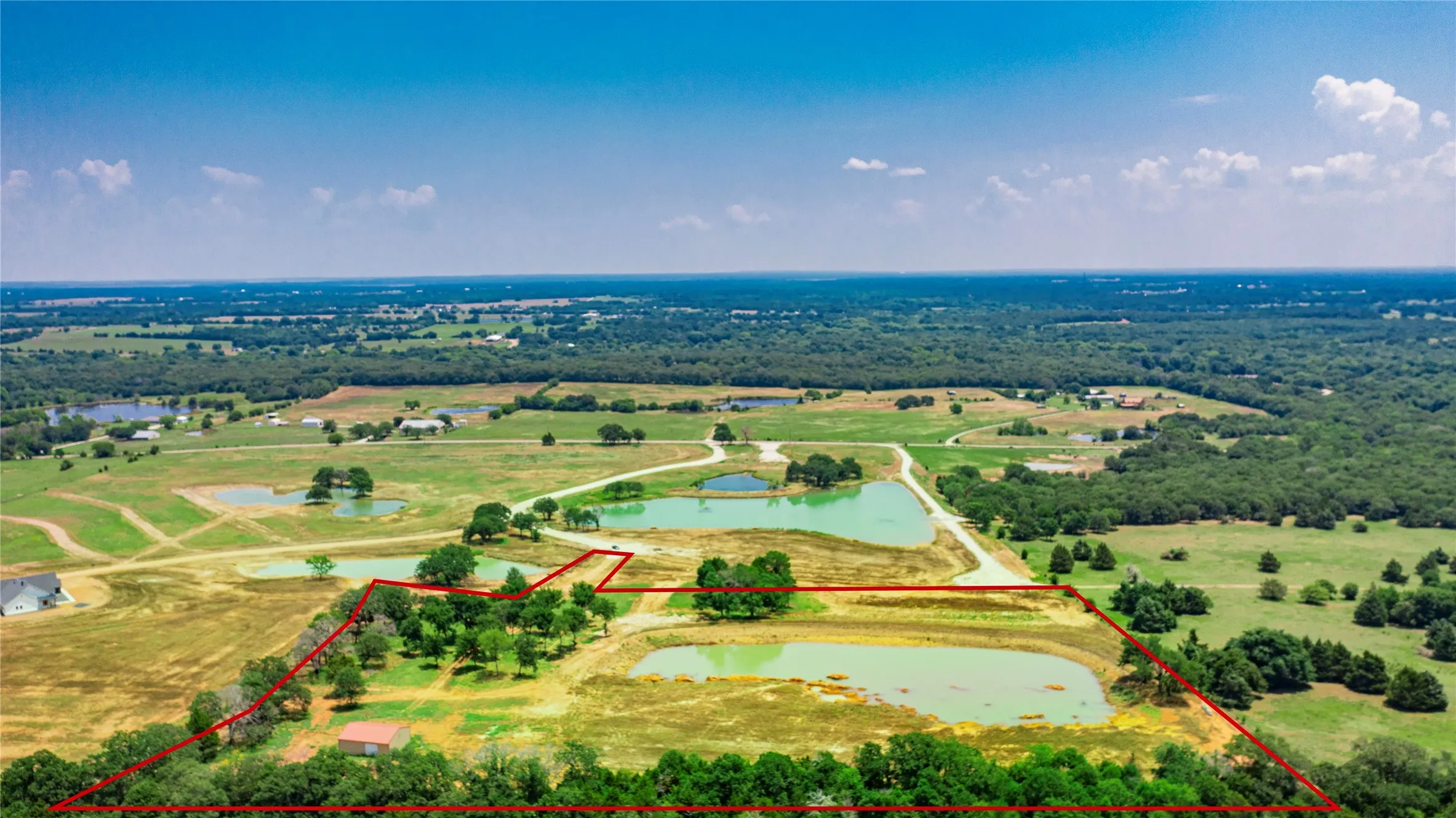 Expansive land parcel featuring multiple ponds, a secluded building, and scattered trees