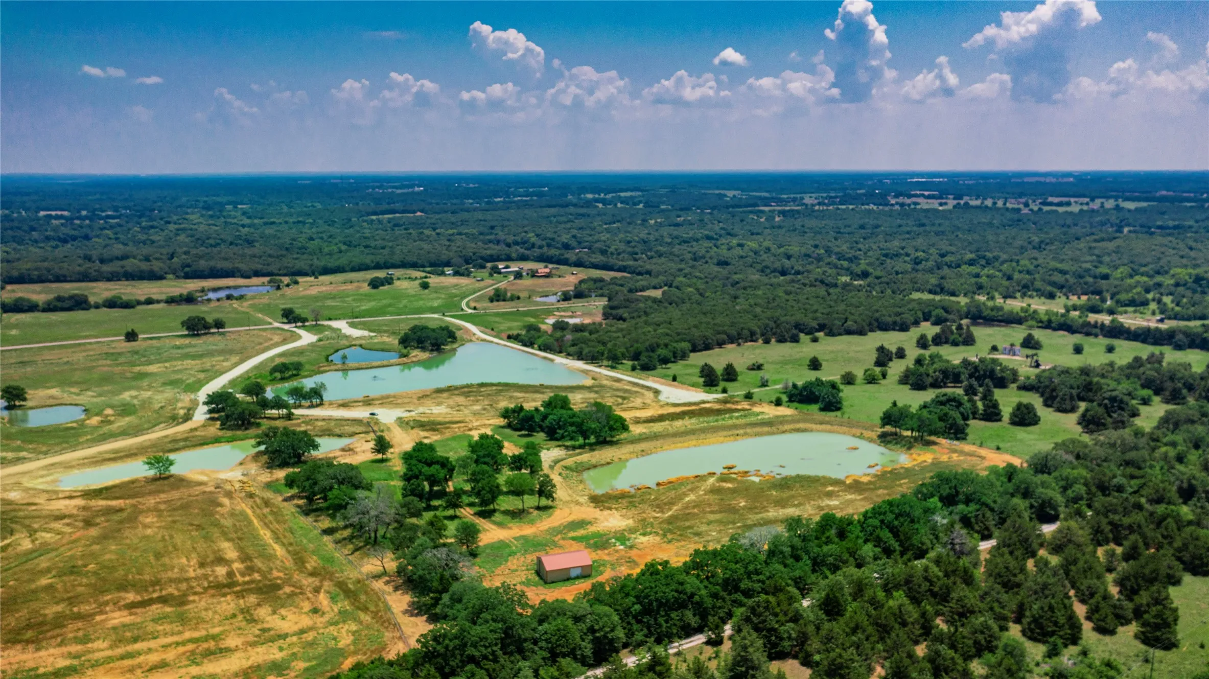 Expansive rural landscape featuring multiple ponds, scattered trees, and a distant red-roofed structure