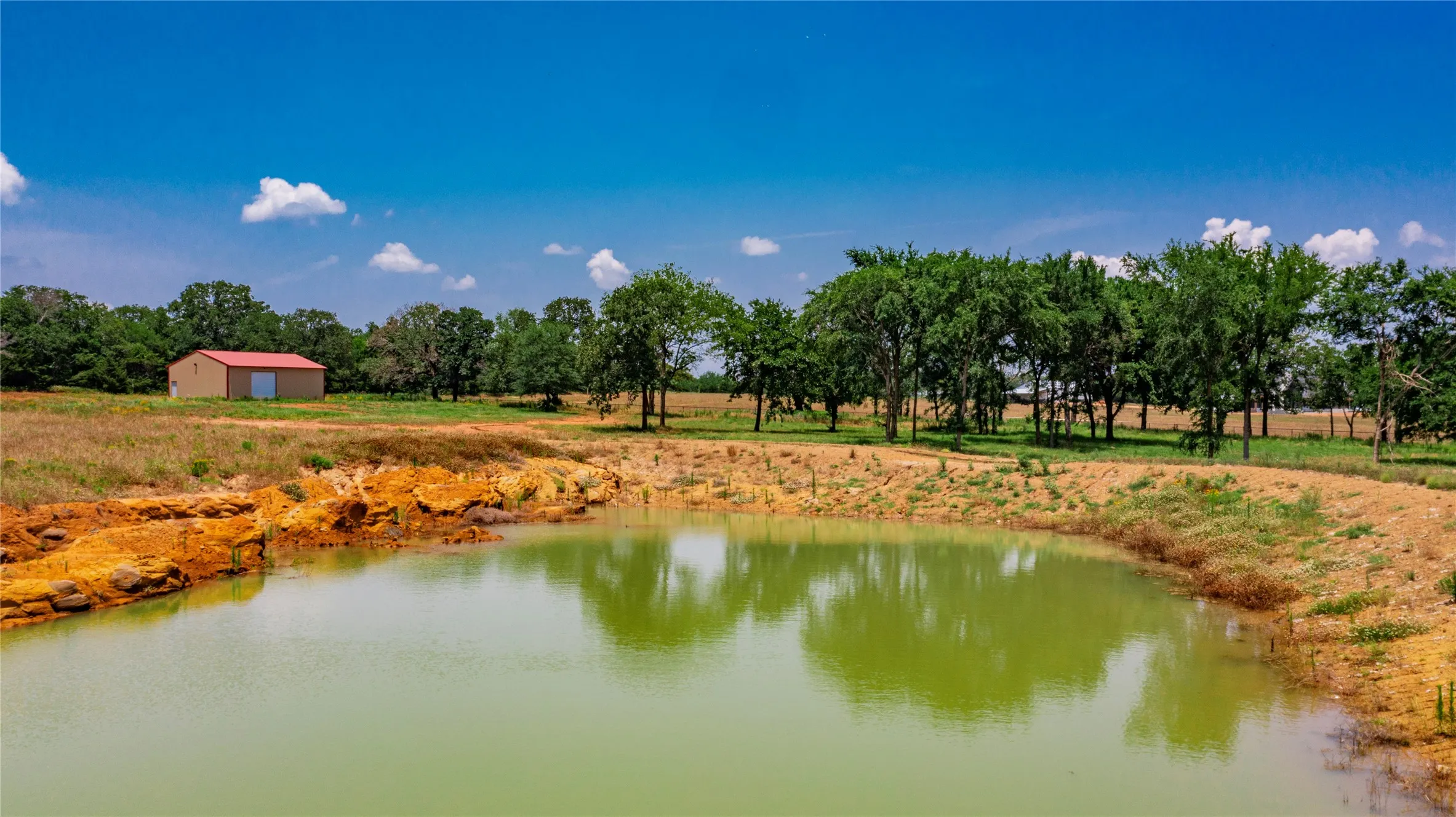 Private pond with earthen banks and a metal-clad building featuring a red roof