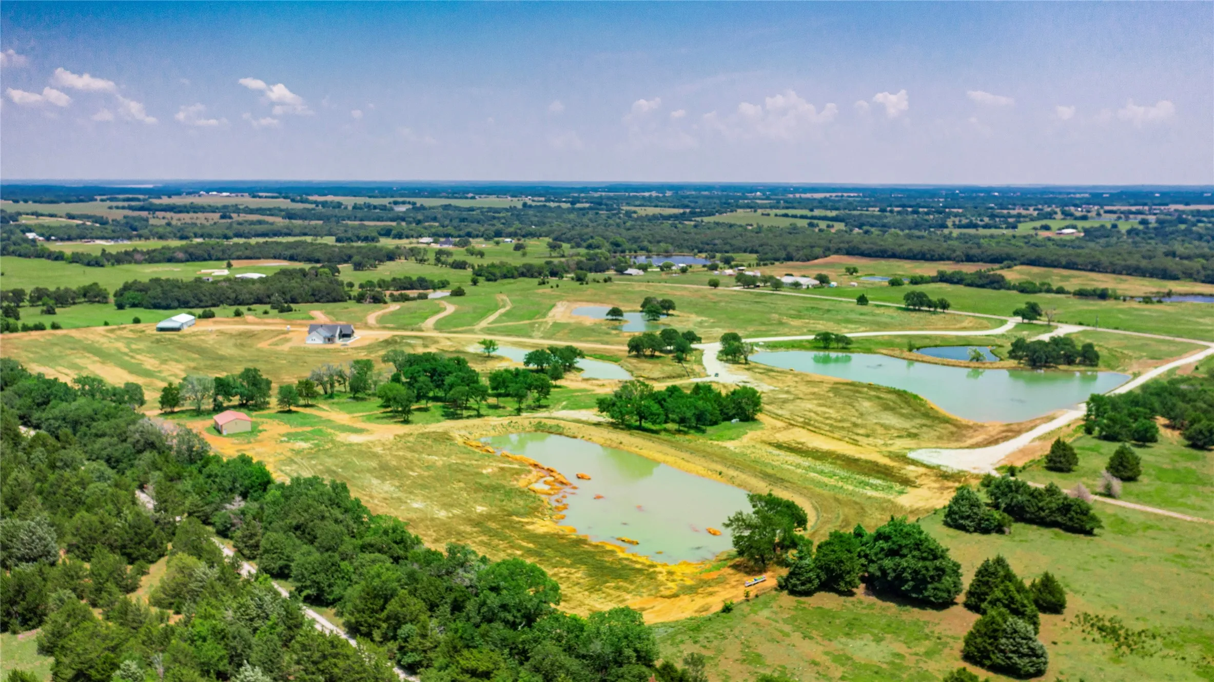 Expansive rural landscape featuring multiple ponds, scattered trees, and a distant residential structure