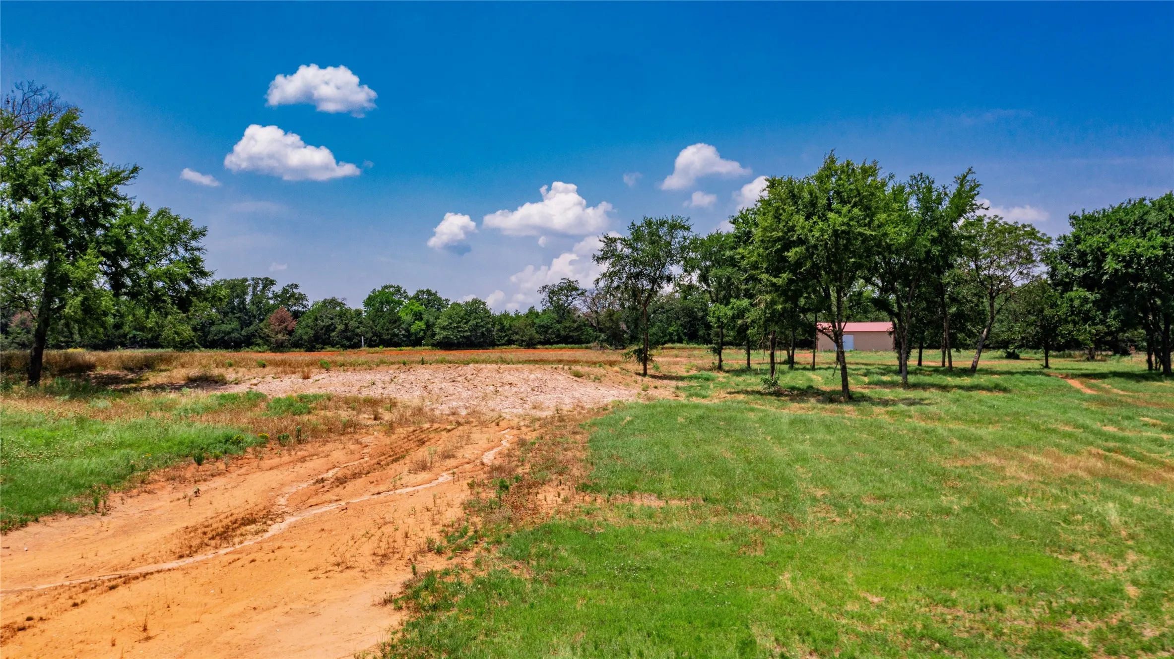 Expansive rural property featuring a mix of cleared land and mature trees, with a visible outbuilding