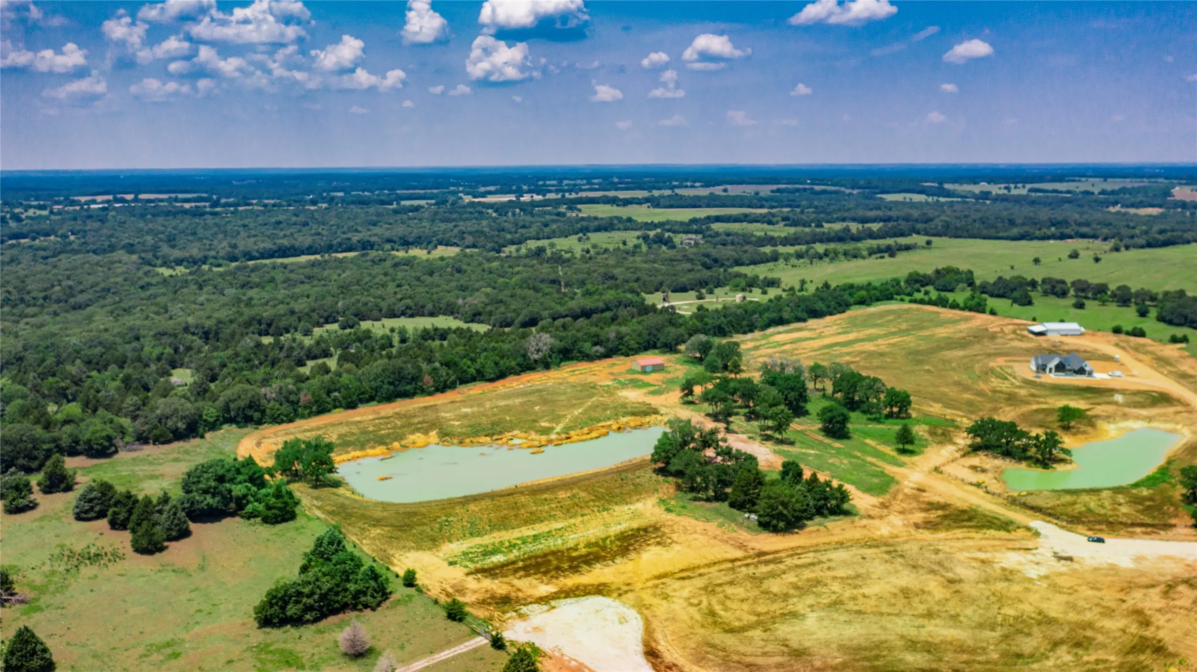 Expansive rural property featuring two ponds, established tree lines, and a distant residence with an accompanying outbuilding