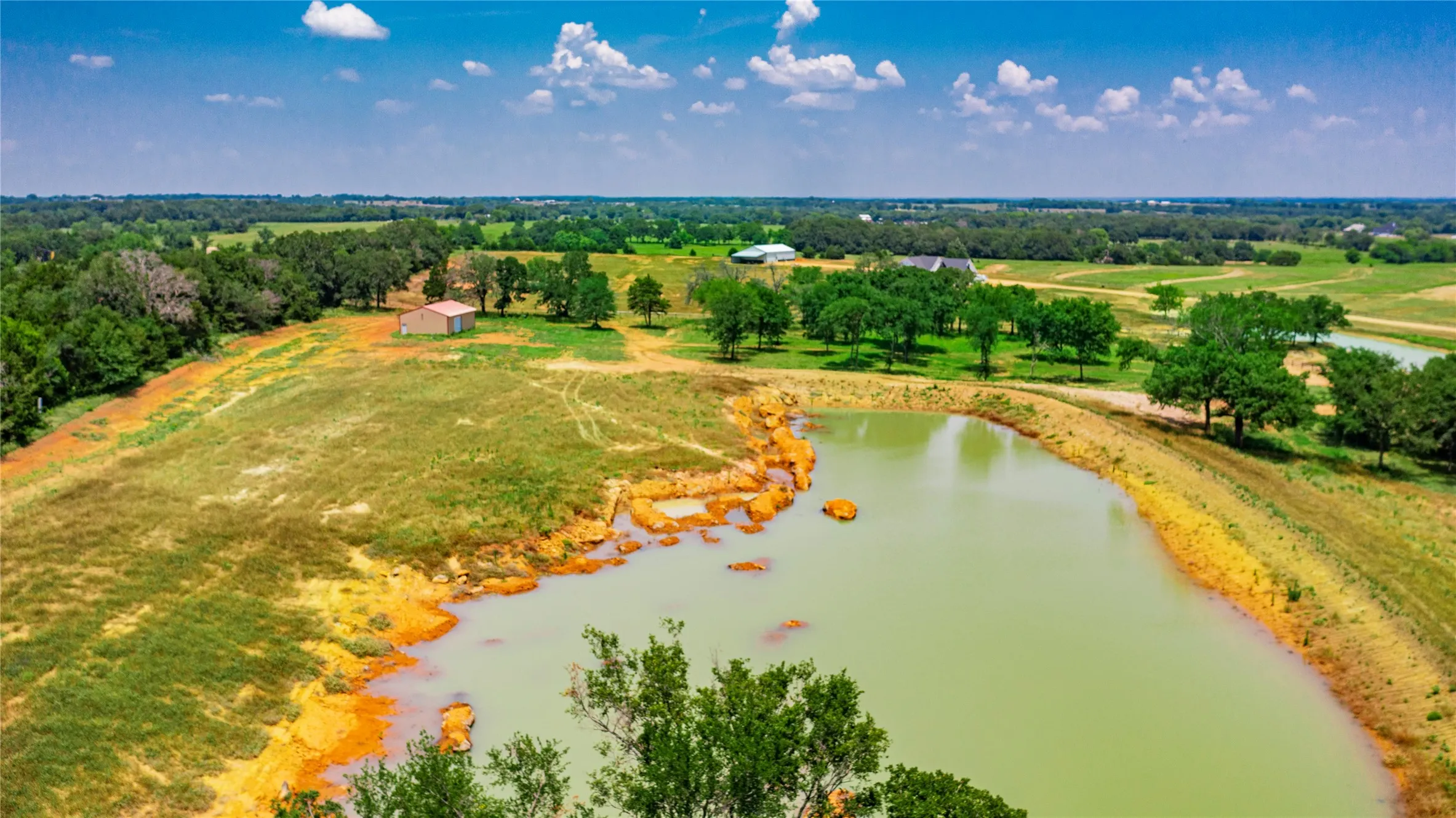 Expansive acreage featuring a substantial pond, mature trees, open fields, and a barn structure