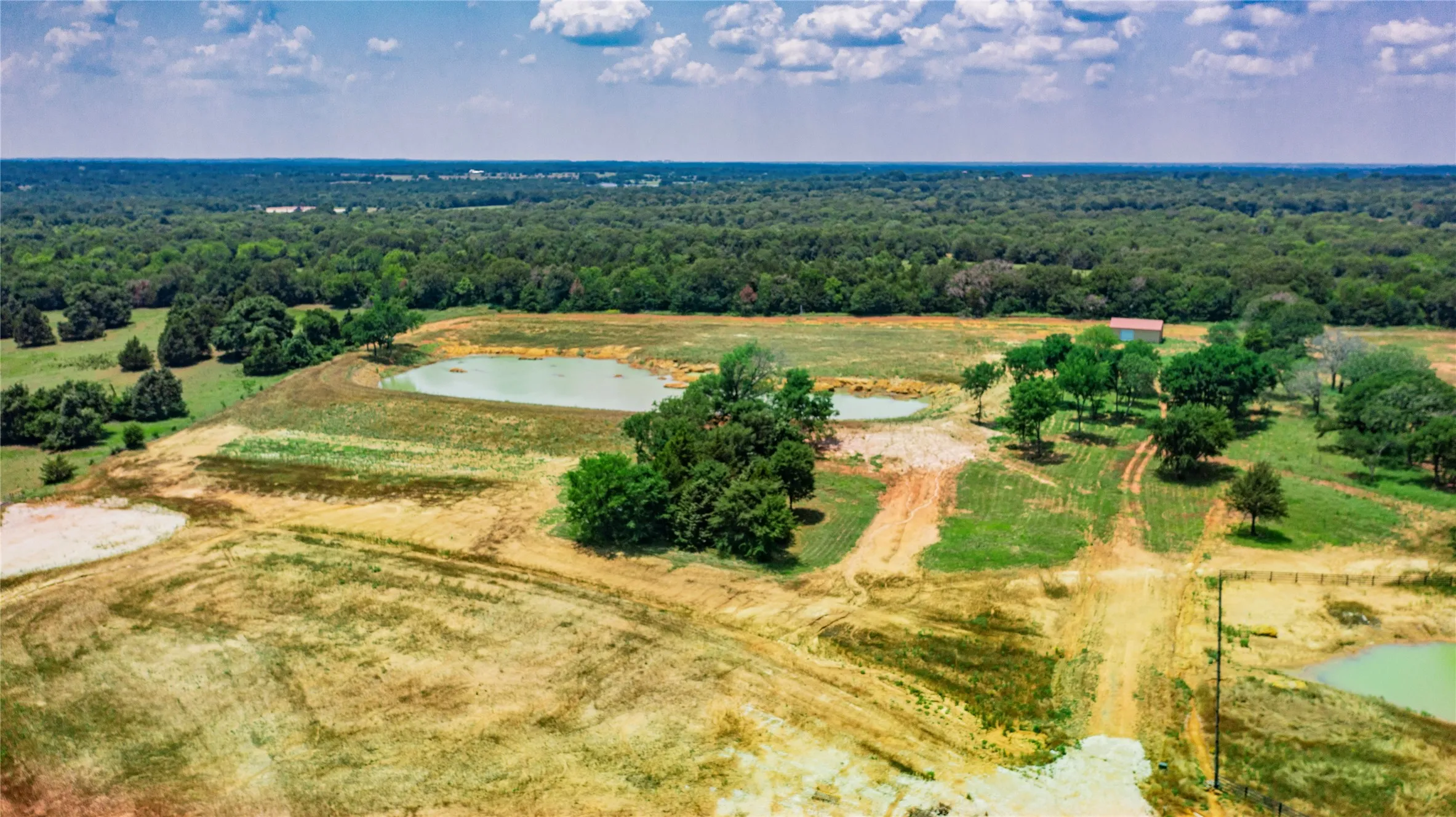 Expansive rural landscape featuring multiple ponds, scattered mature trees, and a distant barn structure