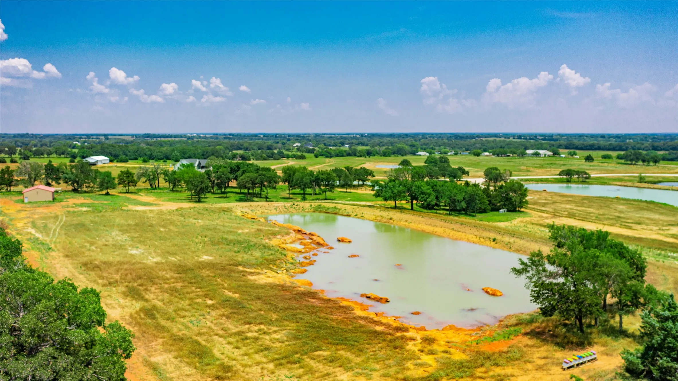 Expansive rural landscape featuring multiple bodies of water, mature trees, and open fields under a clear sky