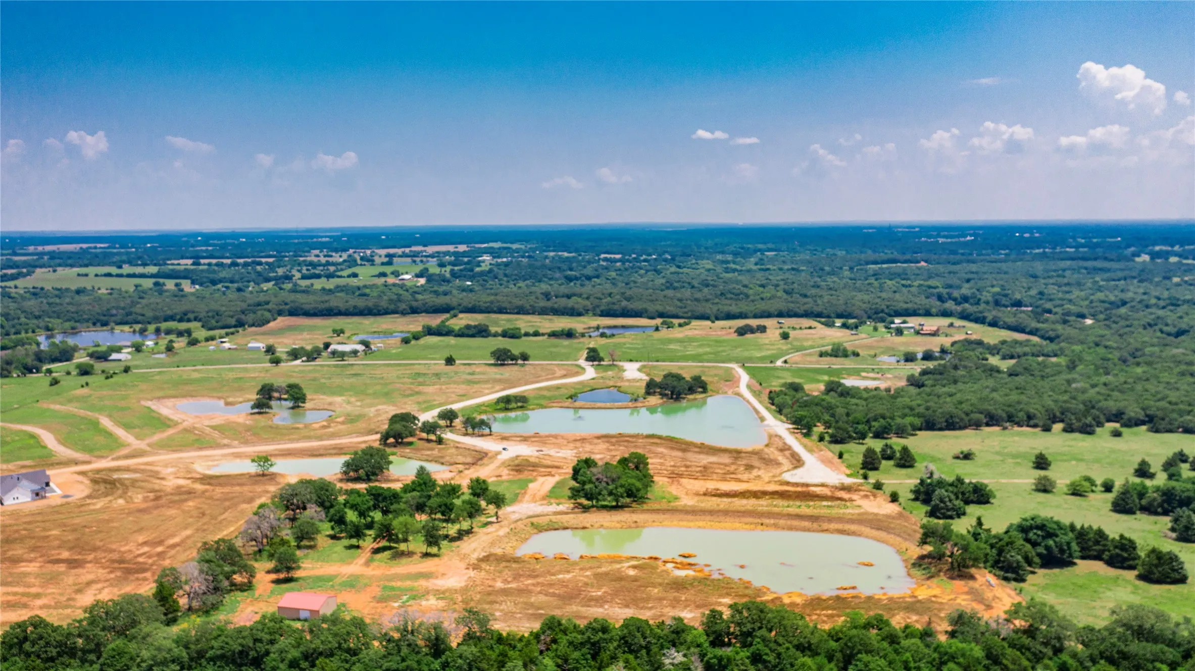 Expansive aerial landscape featuring multiple bodies of water, undeveloped land, and distant structures