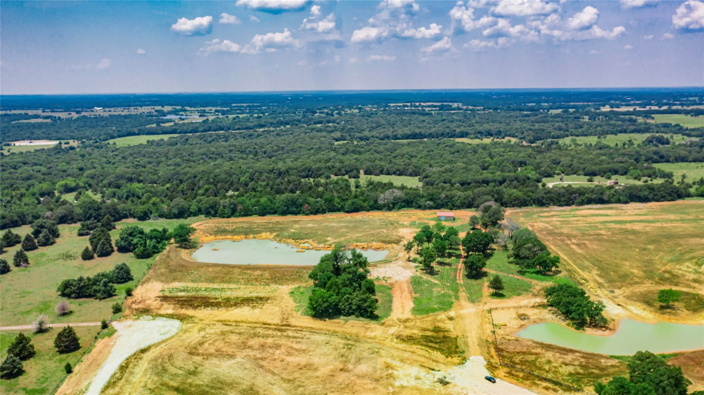 Expansive rural landscape featuring multiple ponds, scattered mature trees, and varying terrain