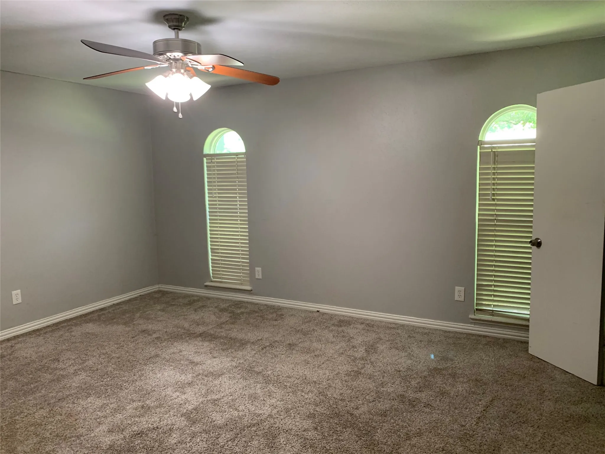 Spacious interior room featuring neutral gray walls, plush carpeting, and a ceiling fan with integrated lighting