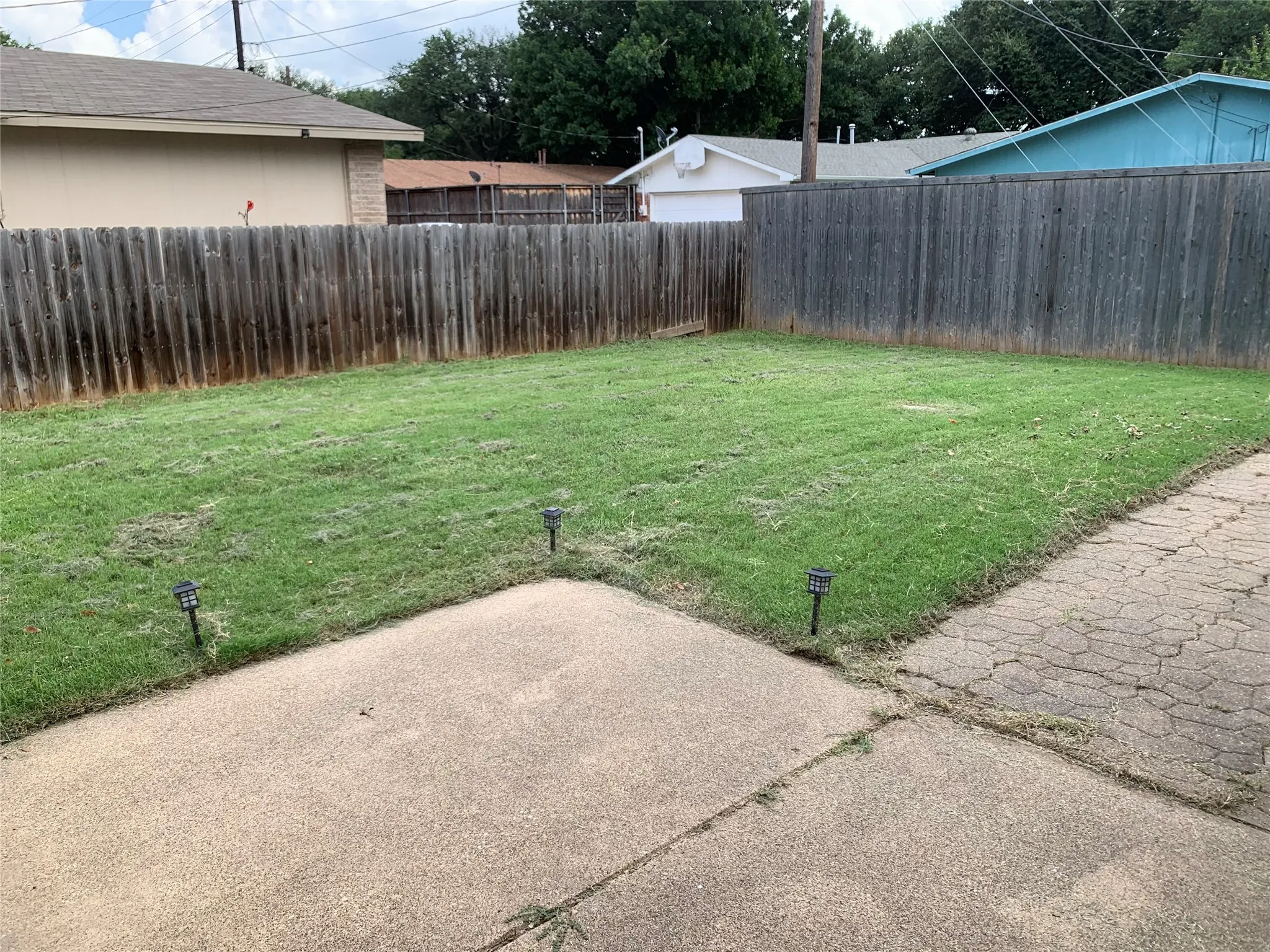 Expansive backyard featuring a wood privacy fence, a concrete patio, and a grass lawn