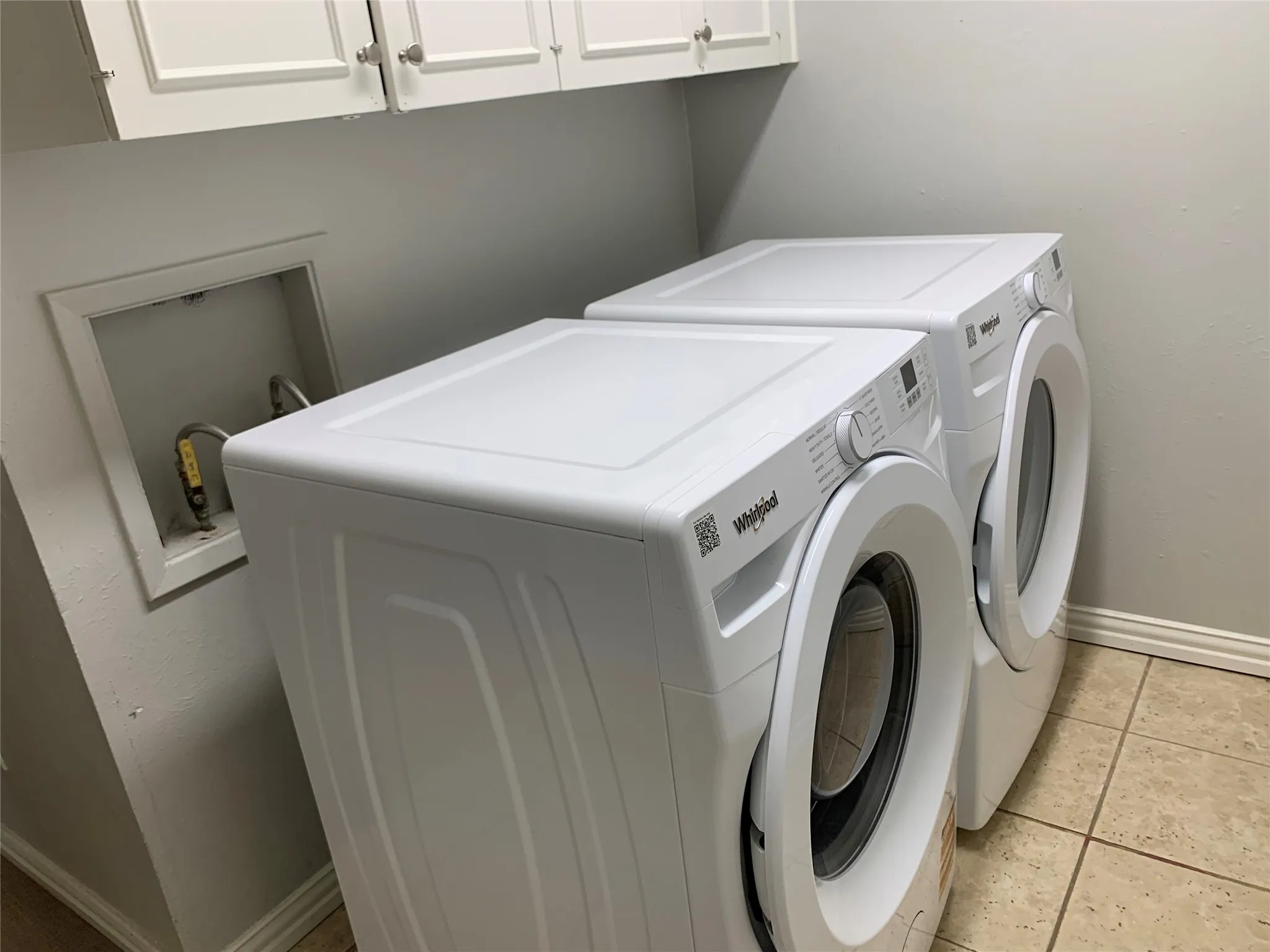 Laundry area featuring overhead white cabinetry with brushed nickel hardware, light neutral wall paint, and square tile flooring
