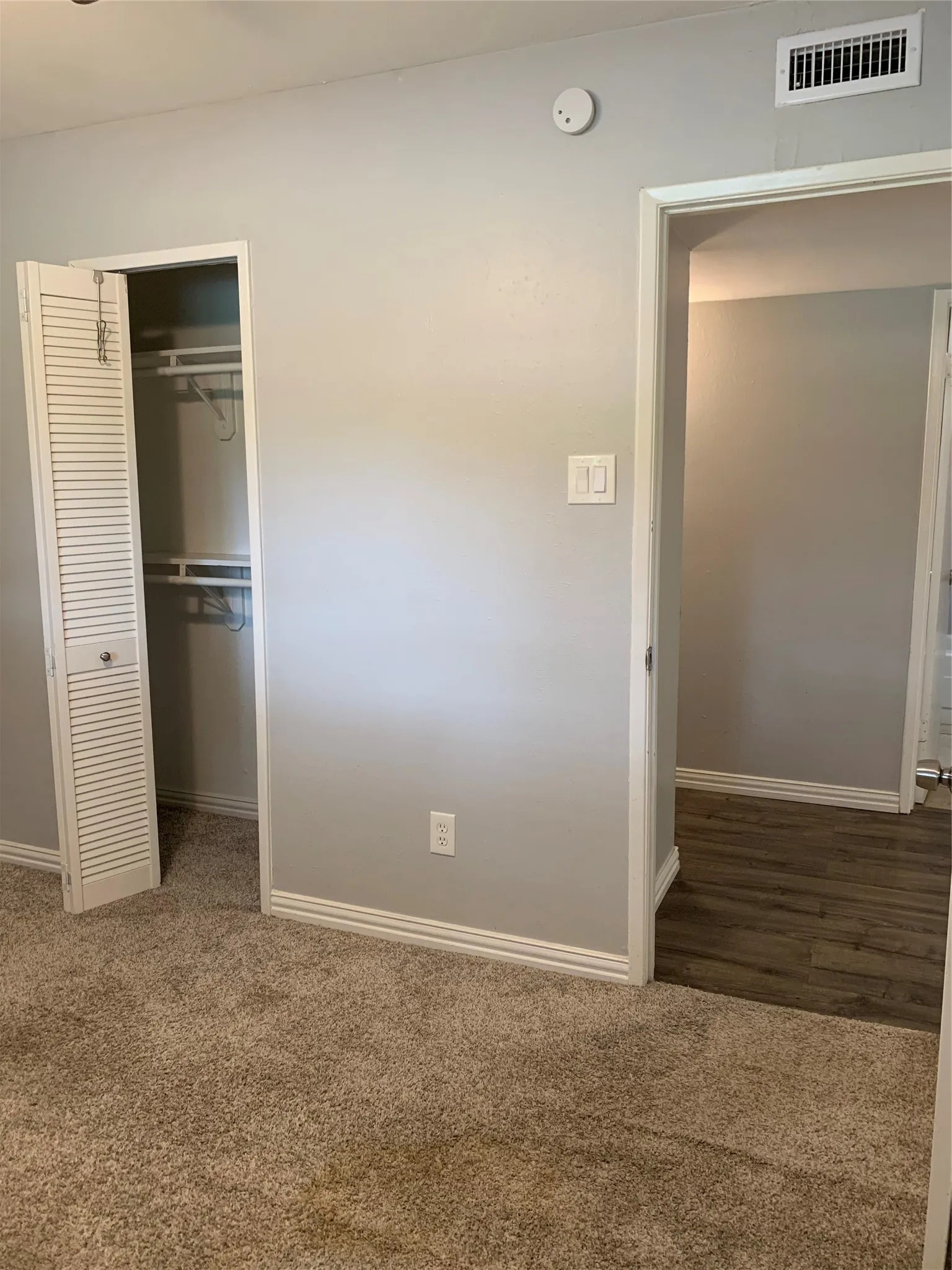 Carpeted interior space featuring a louvered bi-fold closet, light gray wall paint, and white baseboards