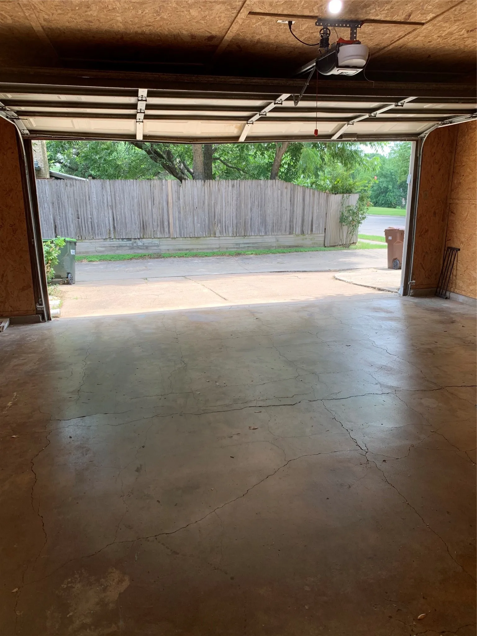 Garage interior featuring an automatic garage door opener, overhead lighting, oriented strand board walls, and a concrete floor