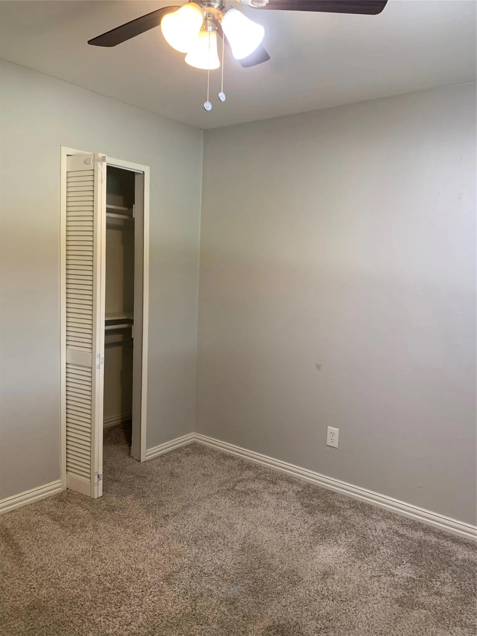 Carpeted room featuring a ceiling fan with integrated lighting, bi-fold louvered closet doors, and white baseboards