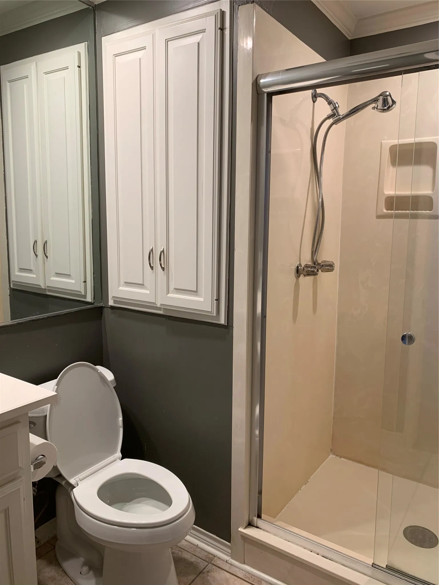 Shower enclosure with sliding glass door, white wall-mounted cabinetry, mirrored wall, and commode