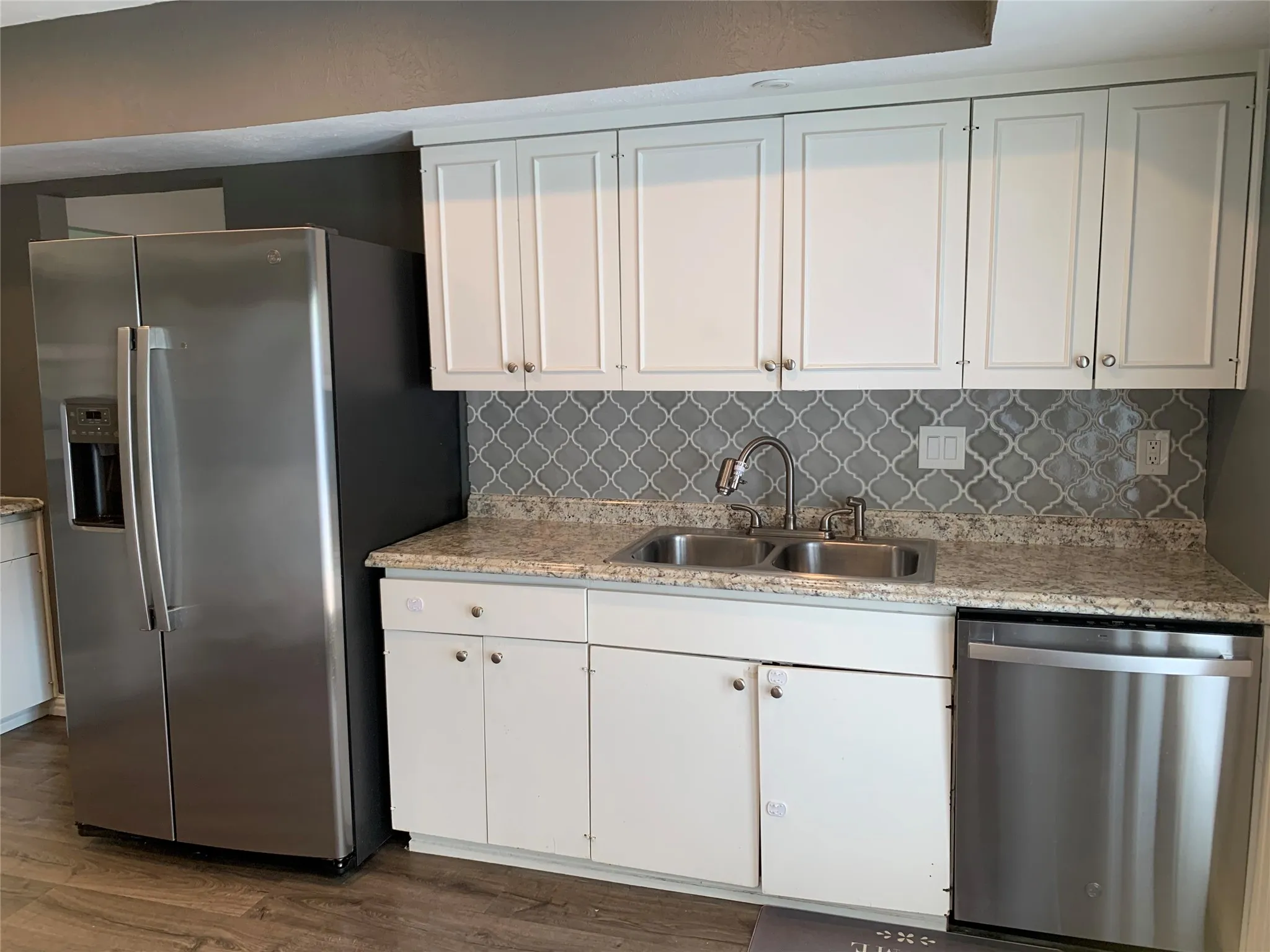 Kitchen featuring white shaker-style cabinetry, a gray arabesque tile backsplash, and light speckled countertops