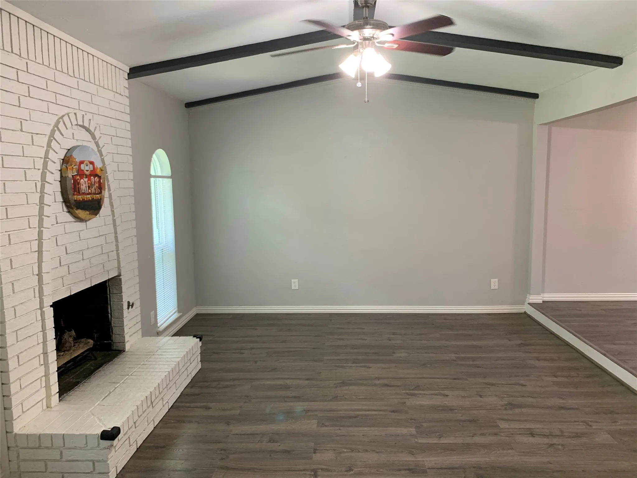 Spacious interior featuring wood-finish flooring, a white brick fireplace with hearth, and an arched window