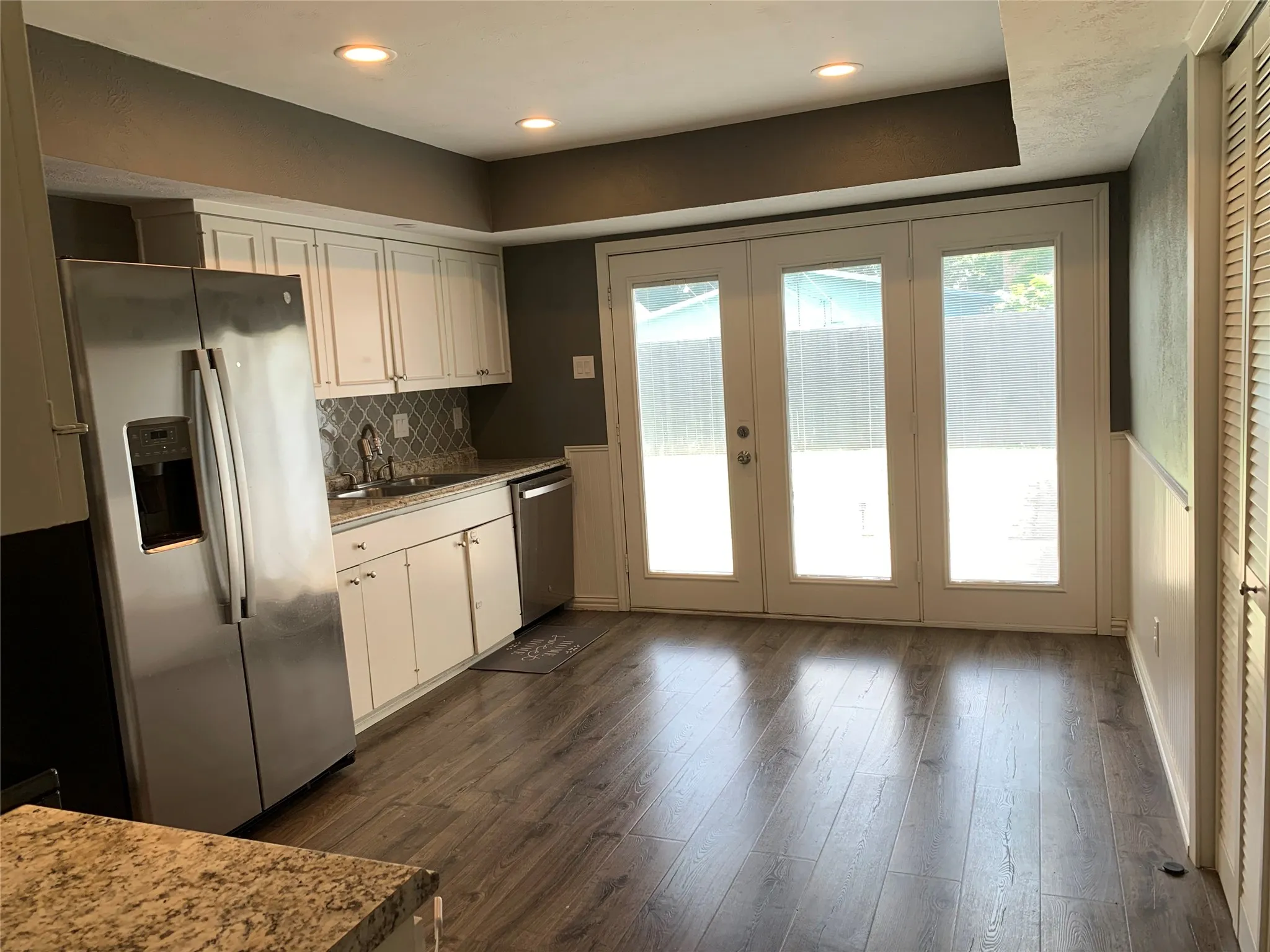 Kitchen area featuring wood-finish flooring, white cabinetry, a patterned backsplash, and recessed lighting