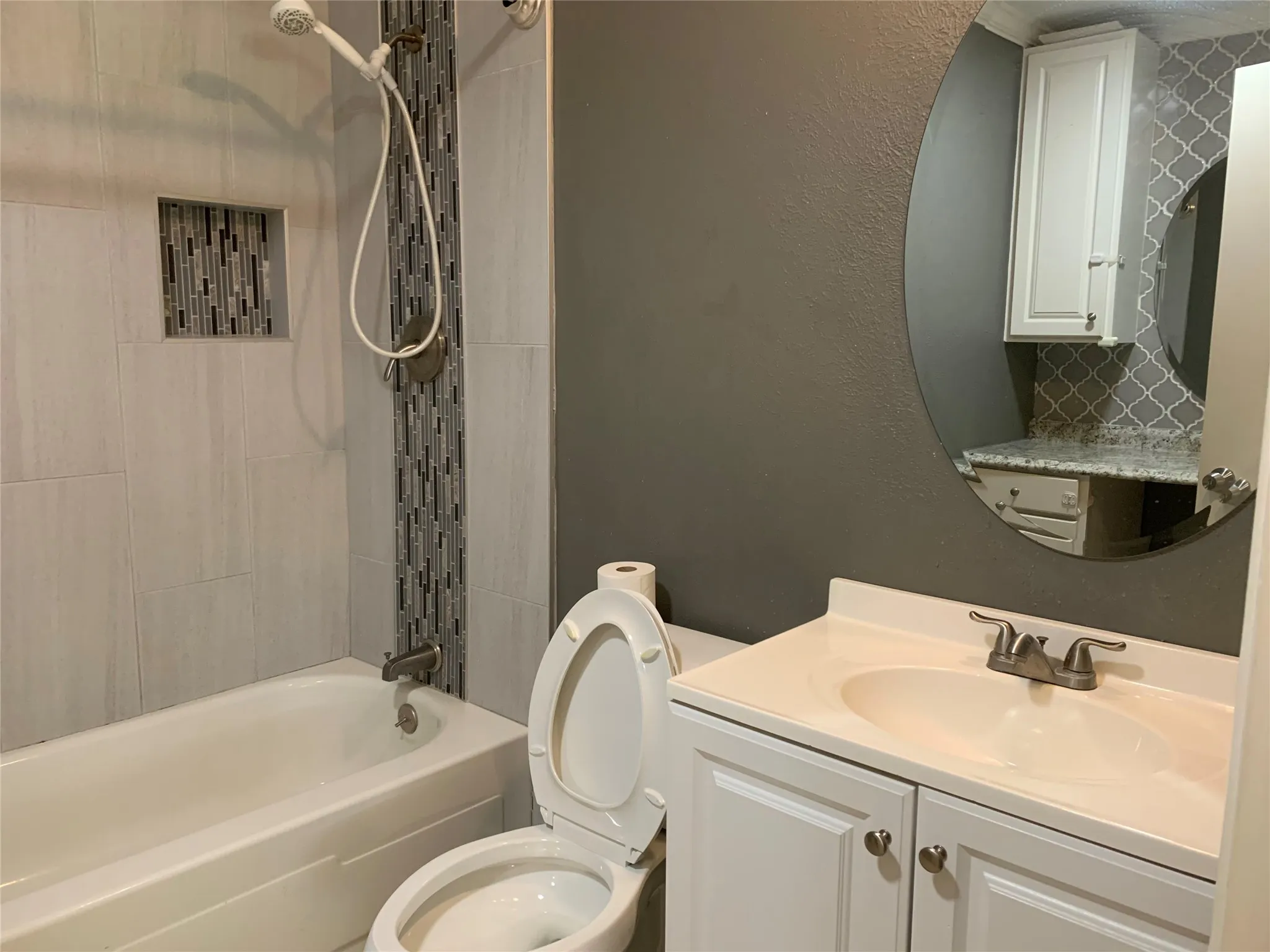Bathroom featuring a white bathtub, tiled shower surround with accent mosaic, recessed shower niche, white vanity with integrated sink, and an oval mirror
