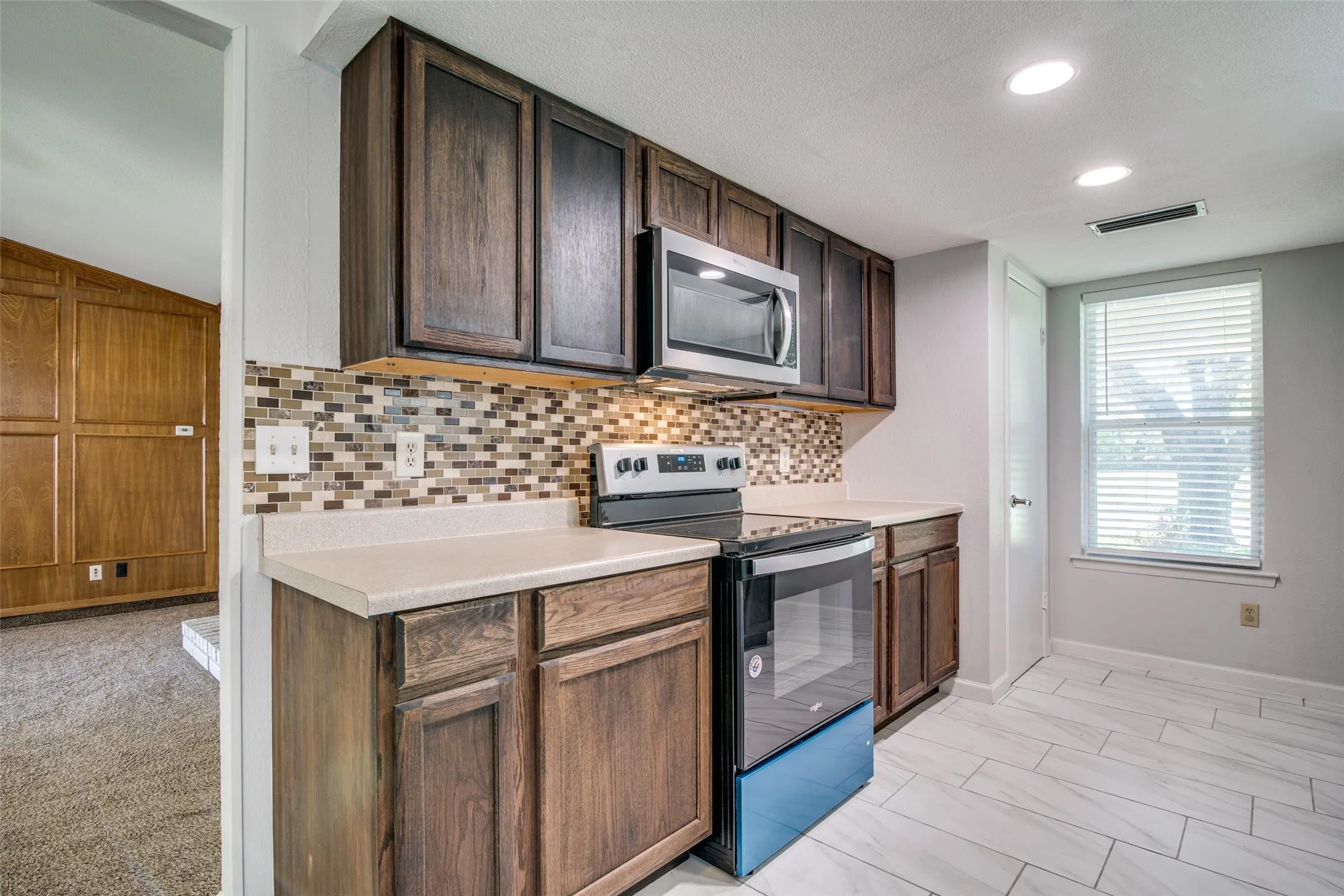 Kitchen featuring dark wood-finish cabinetry, light-toned countertops, and a mosaic tile backsplash