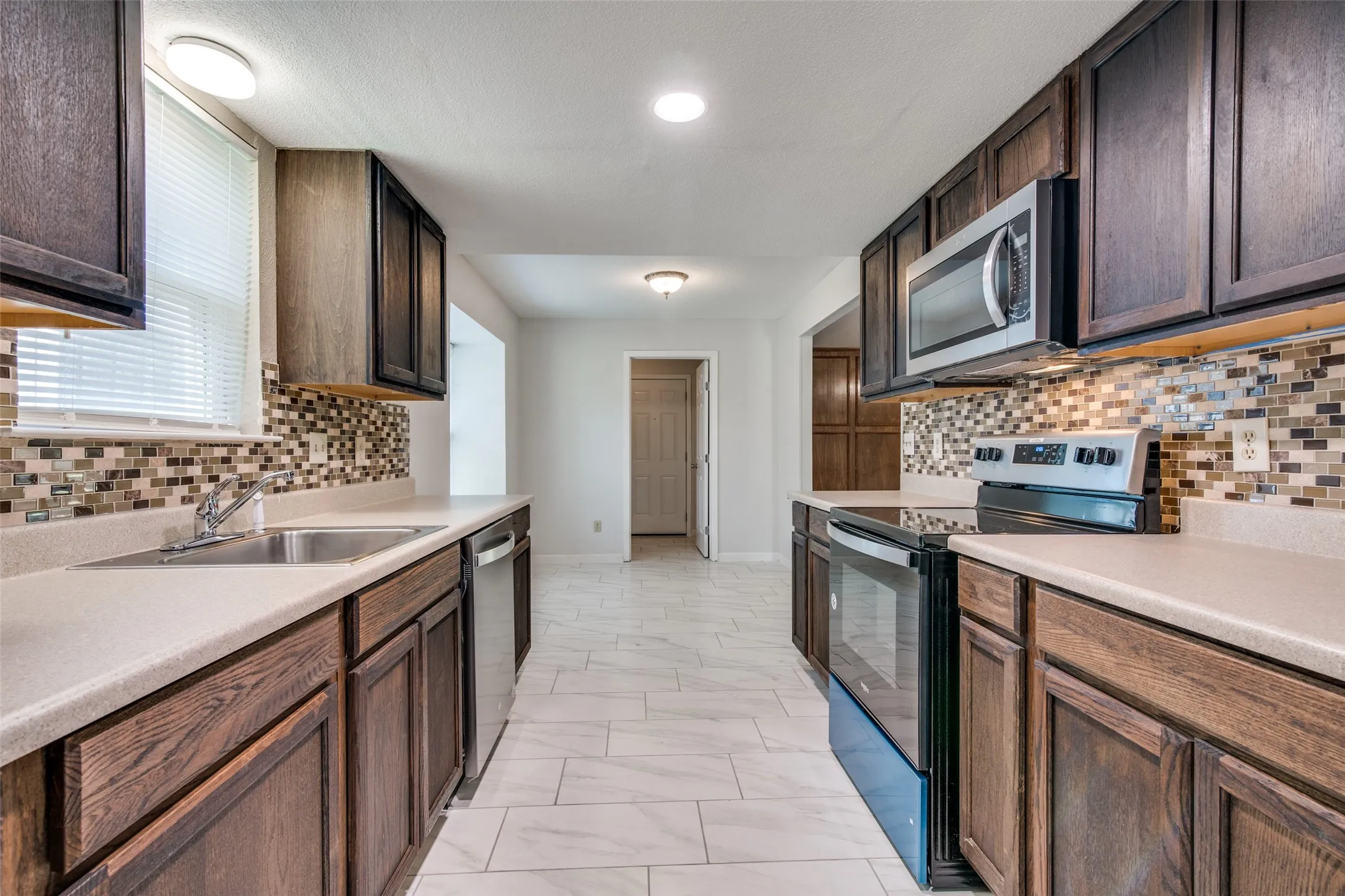 Kitchen featuring dark wood cabinetry, light countertops, mosaic tile backsplash, stainless steel appliances, and tile flooring