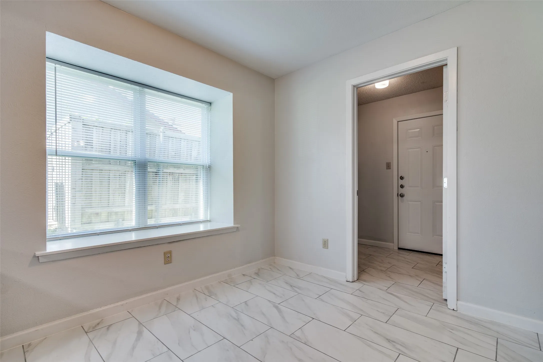 Room featuring a large window with horizontal blinds, light-toned walls, and white baseboards