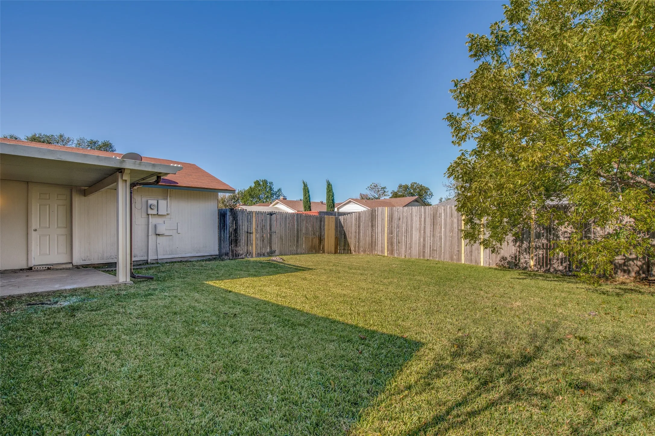Expansive backyard featuring a large green lawn, full wood privacy fence, and covered patio area