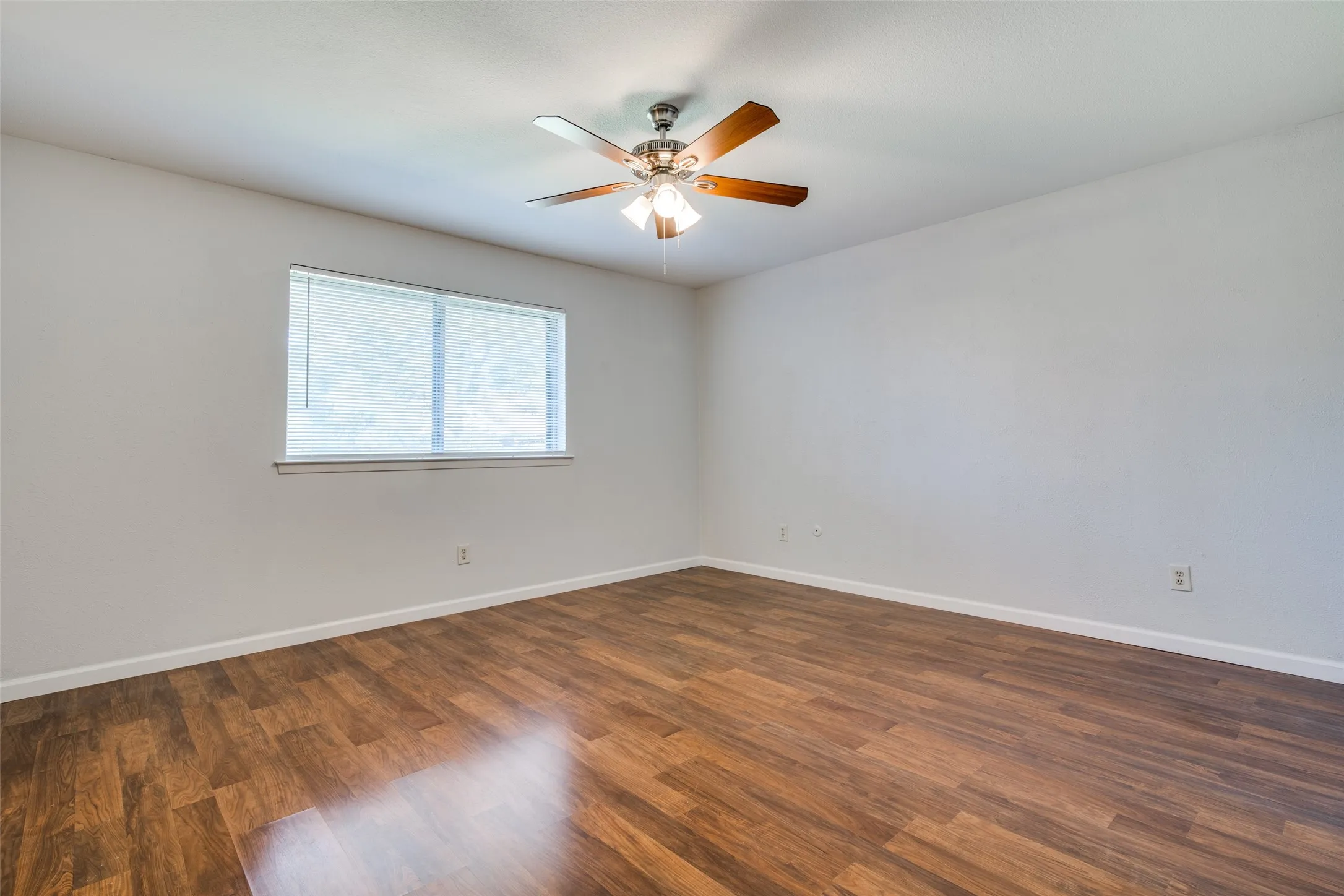 Spacious room featuring wood-finish flooring and a ceiling fan with integrated lighting