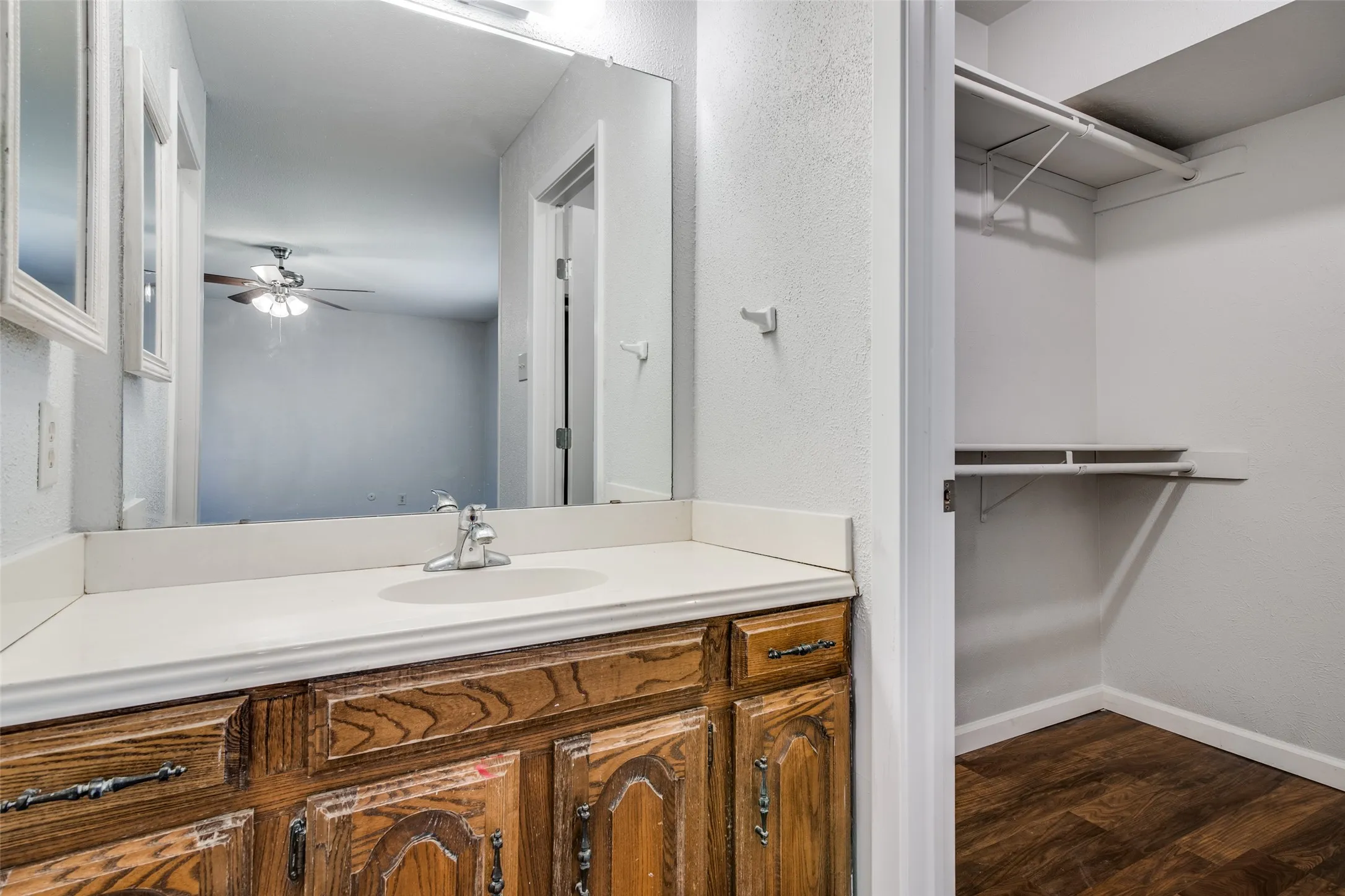 Bathroom vanity featuring a single basin sink, white countertop, and wood-finish cabinetry with decorative hardware
