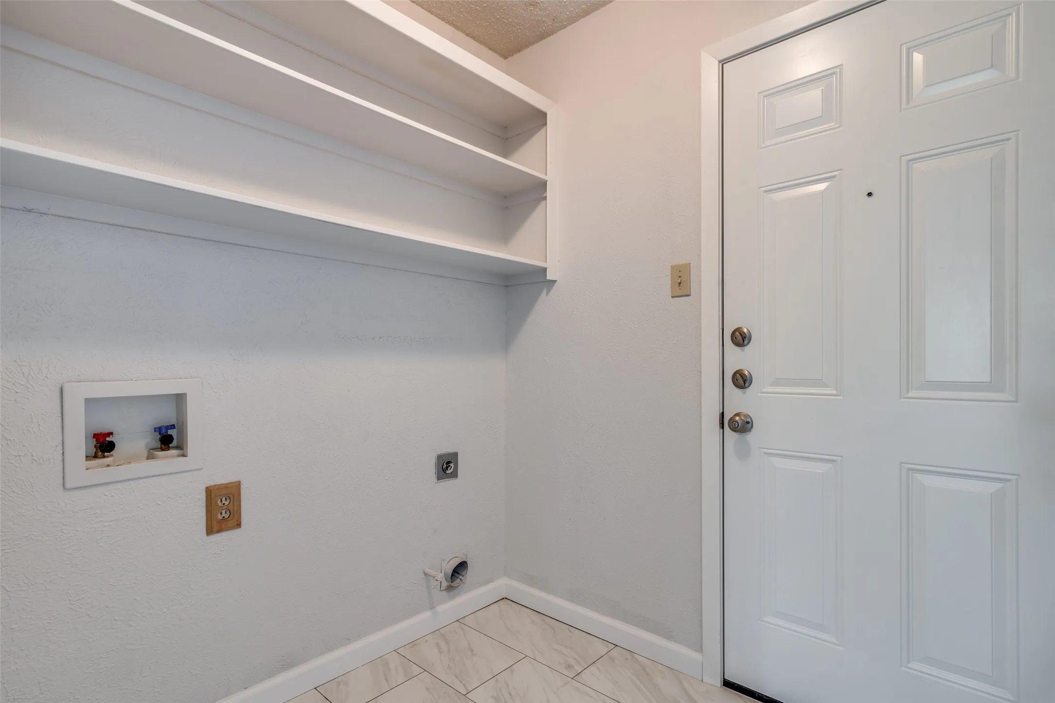 Laundry area with white built-in shelving, white paneled door, and light-toned tile flooring