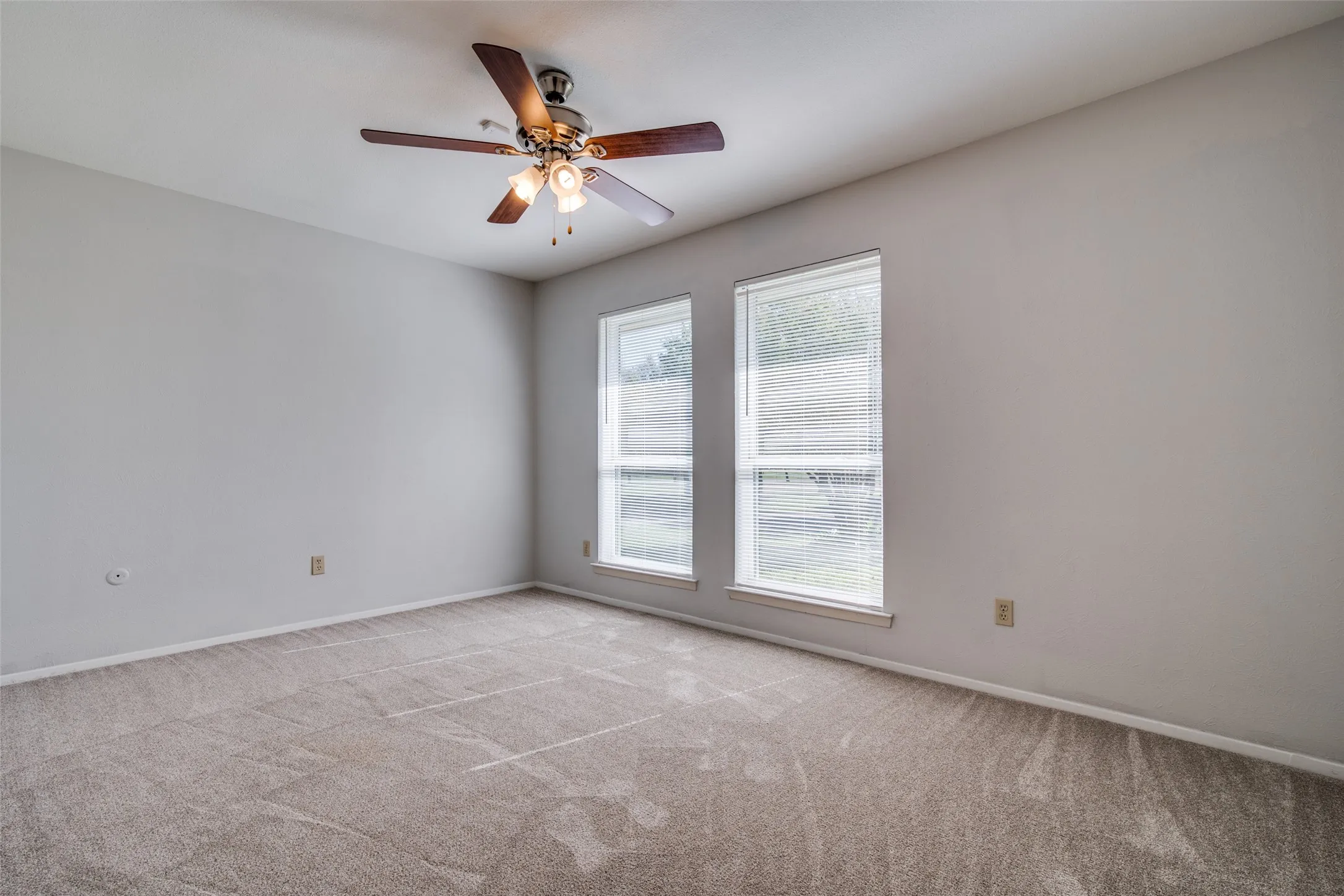 Spacious room featuring neutral carpeting, light gray wall paint, and two large windows with blinds