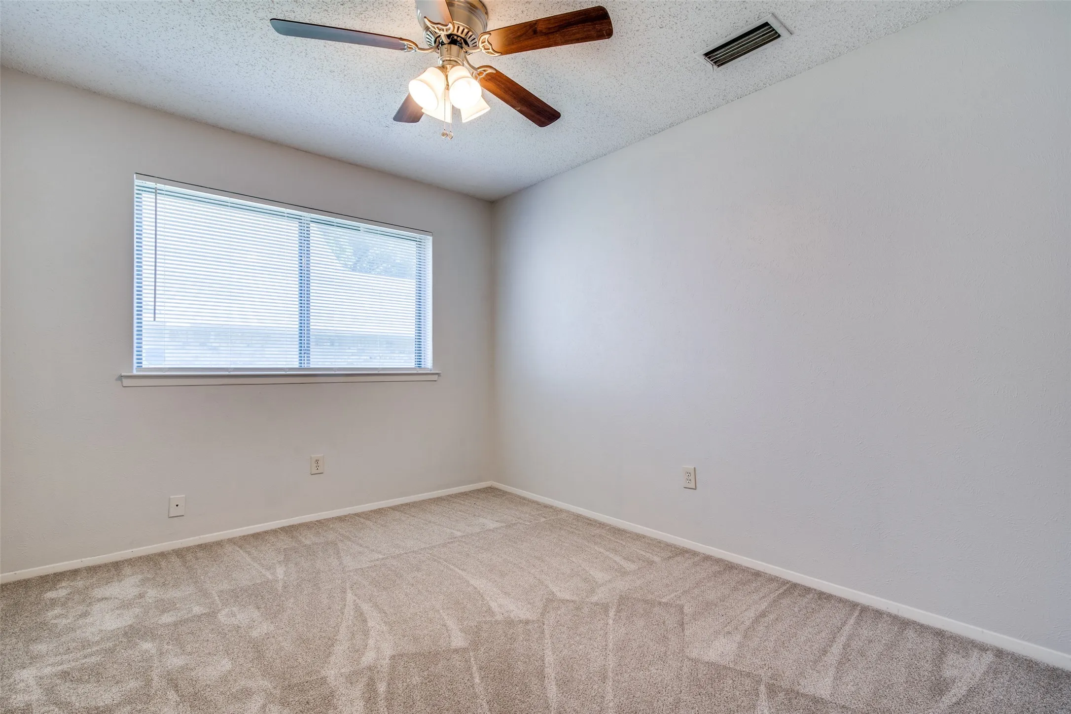 Carpeted room featuring a ceiling fan with integrated lighting, a rectangular window with blinds, and light-toned wall paint