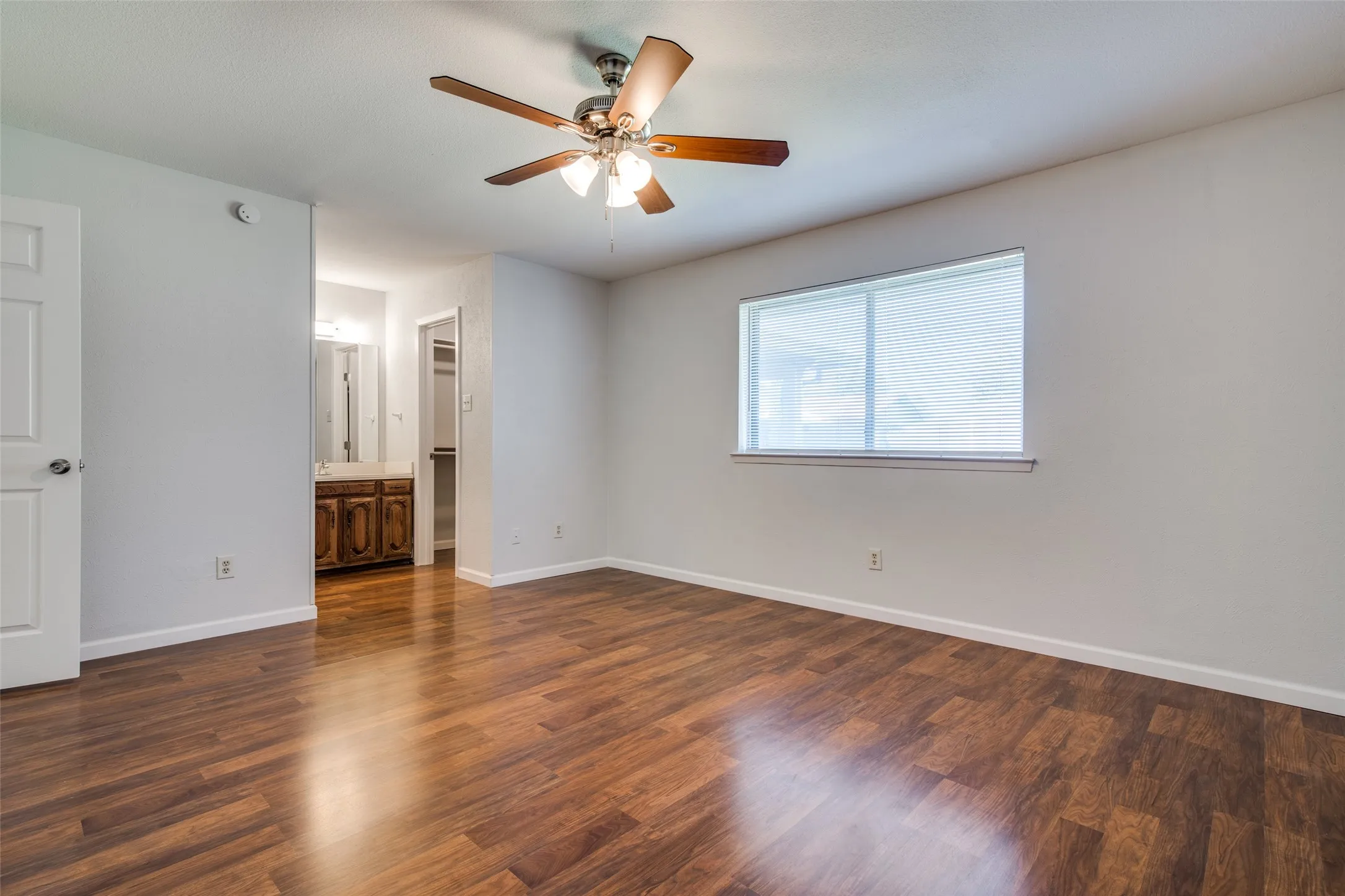 Spacious room featuring wood-finish flooring, a ceiling fan with integrated lighting, and a large window