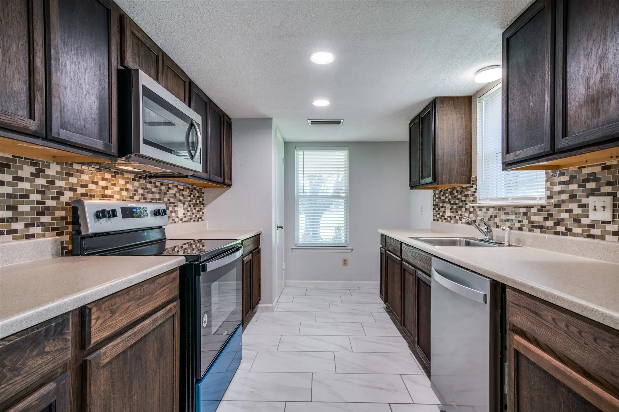 Kitchen featuring dark wood cabinetry, light-toned countertops, and a mosaic tile backsplash