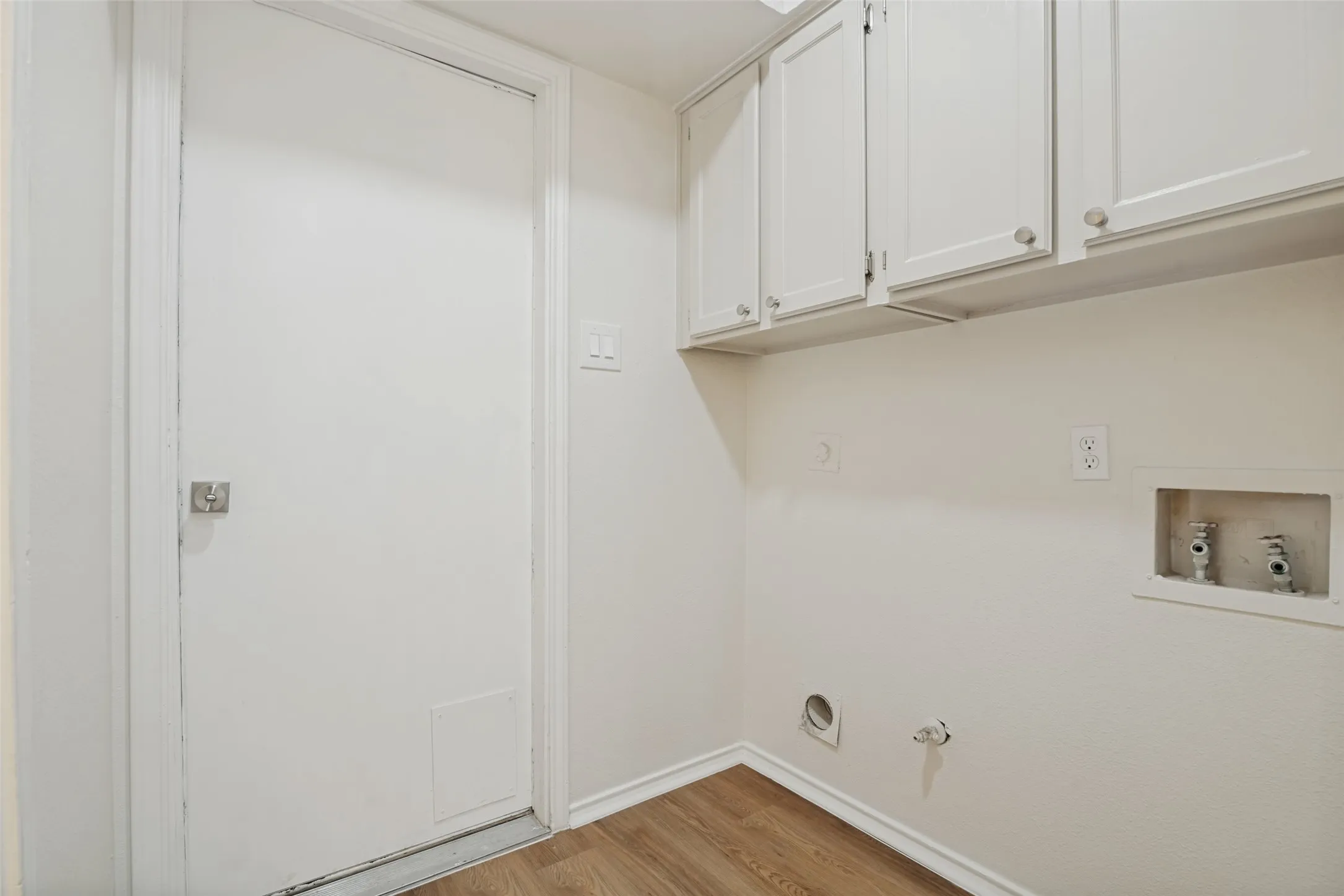 Utility space featuring wood-finish flooring and upper cabinetry