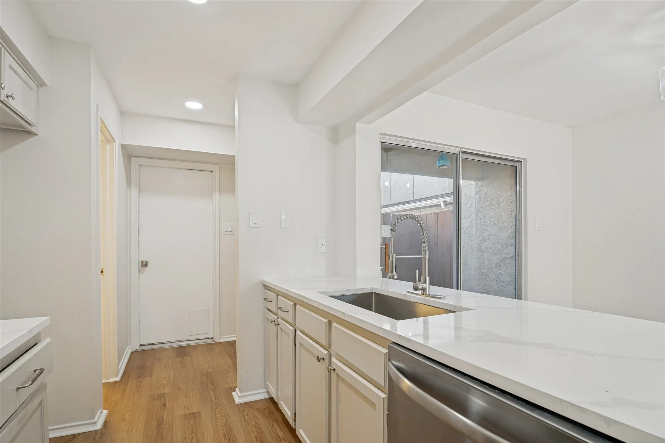 White kitchen featuring extensive counter space, recessed lighting, wood-finish flooring, stainless steel dishwasher, and a stainless steel sink with a pull-down faucet