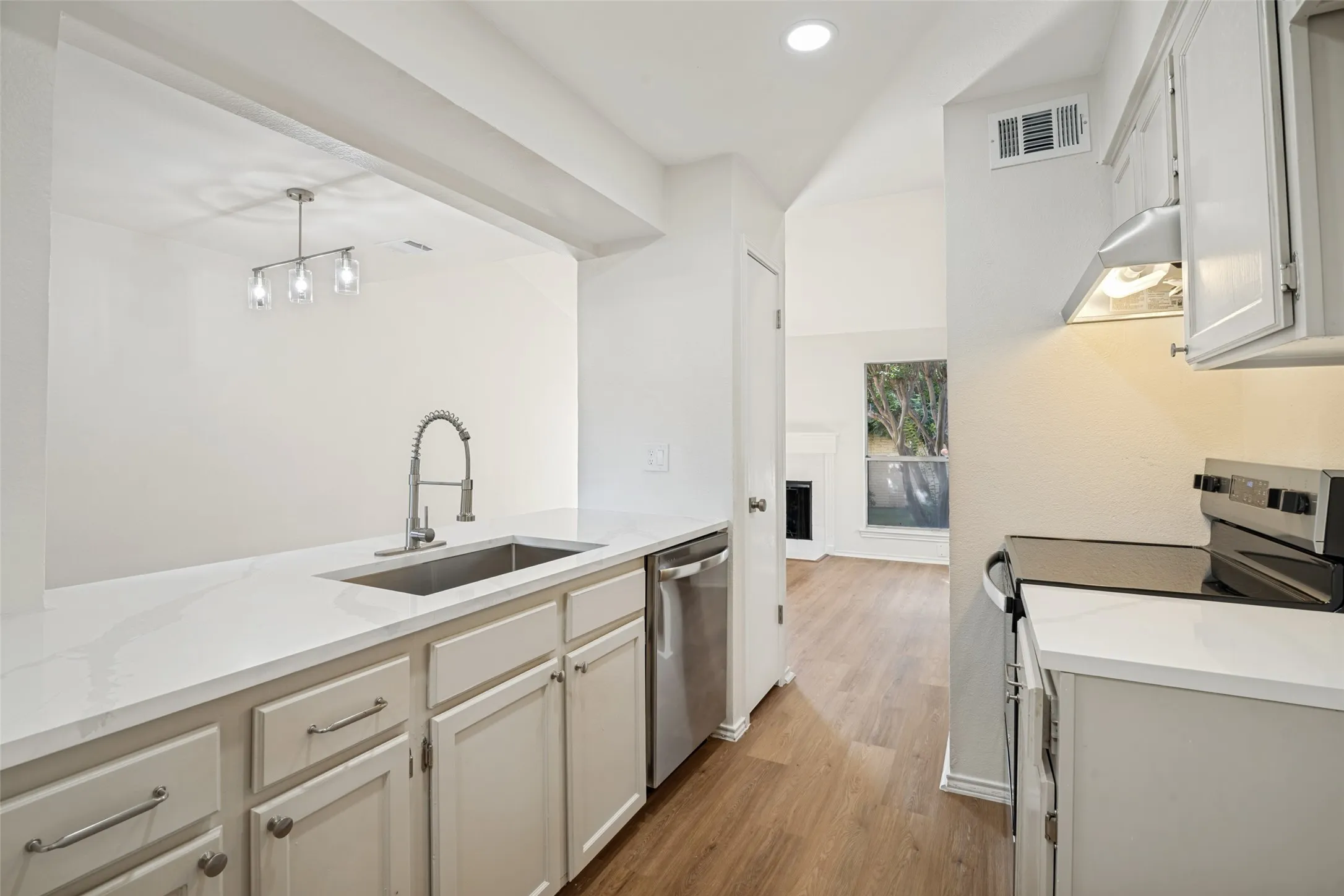 Kitchen featuring white cabinetry, light-toned countertops, a stainless steel sink with a gooseneck faucet, a built-in dishwasher, and wood-finish flooring