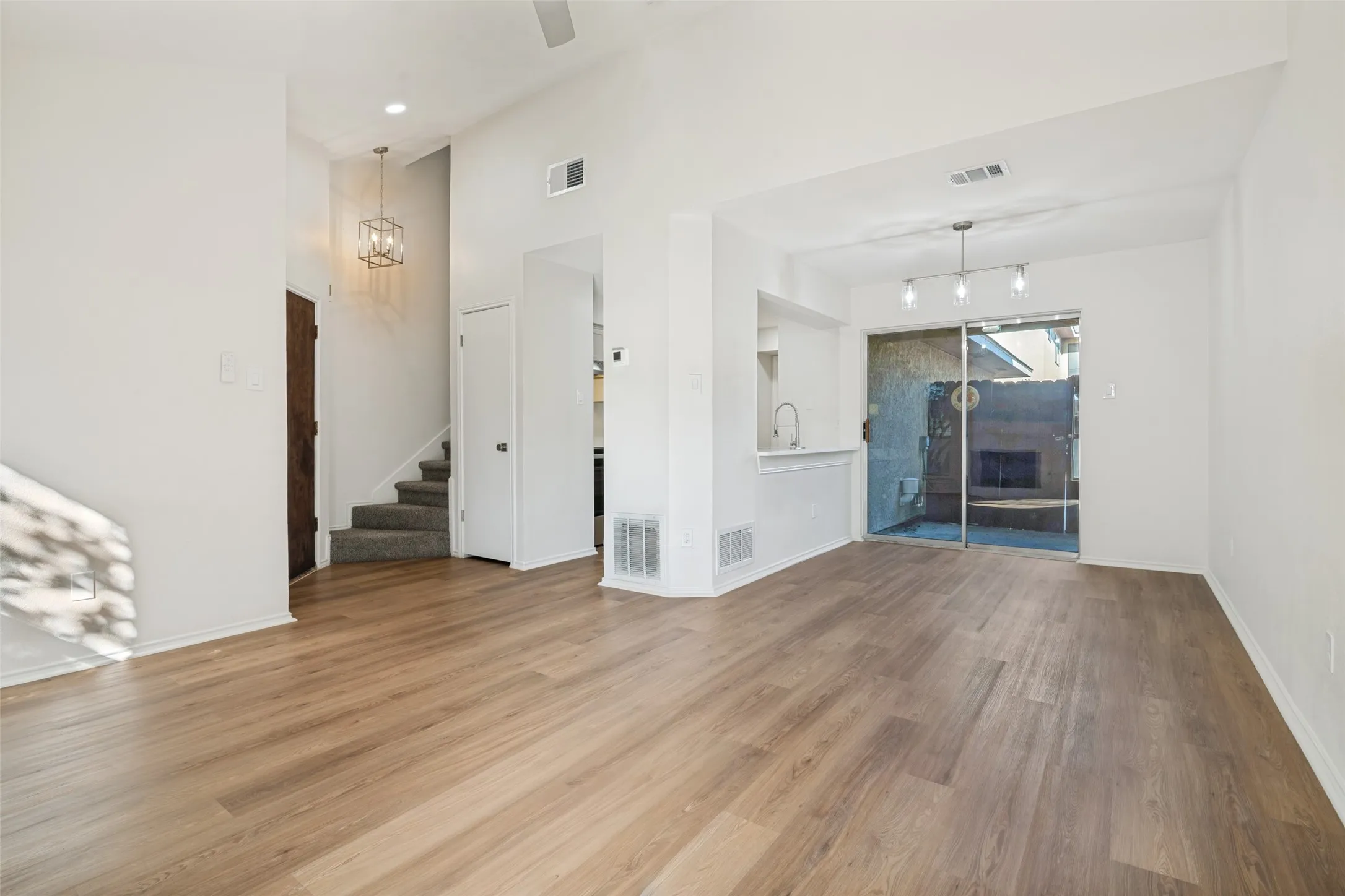 Open-concept main living area featuring wood-finish flooring, high ceilings with a ceiling fan, and sliding glass doors to an outdoor patio