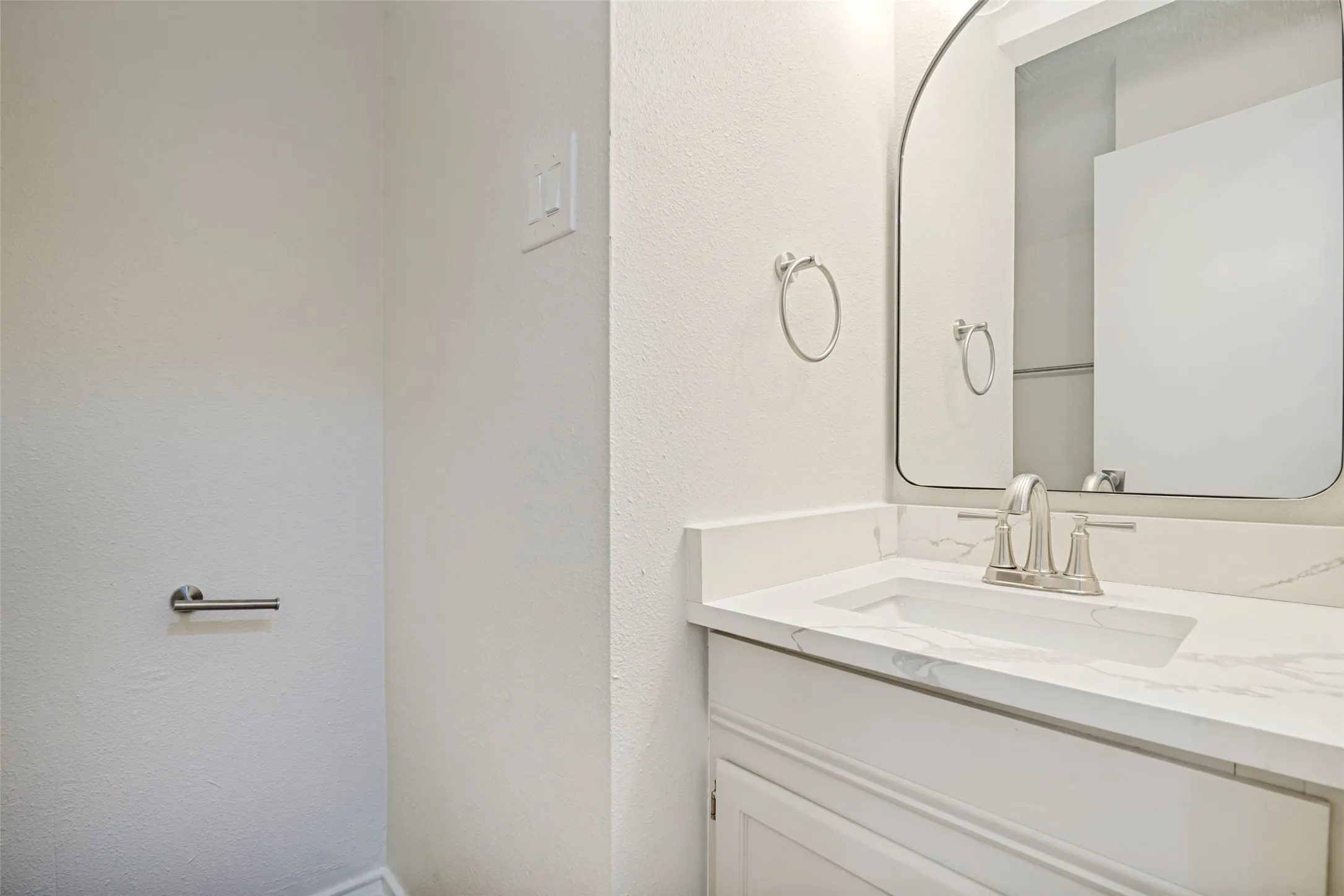 Bathroom vanity featuring a rectangular undermount sink, a stone-finish countertop, and a brushed nickel faucet