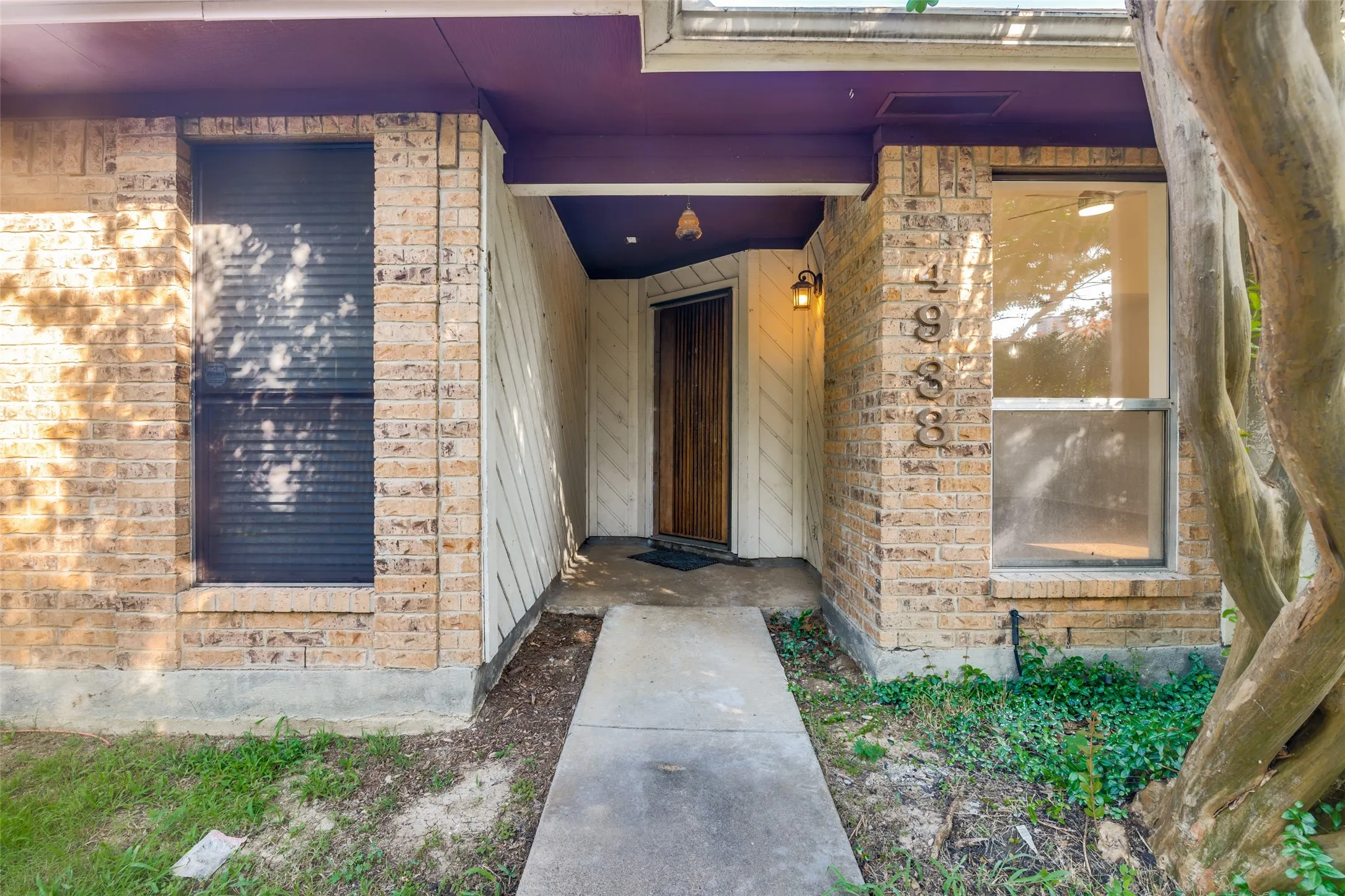 Brick exterior featuring a covered entry, wood door, and an exterior wall light fixture