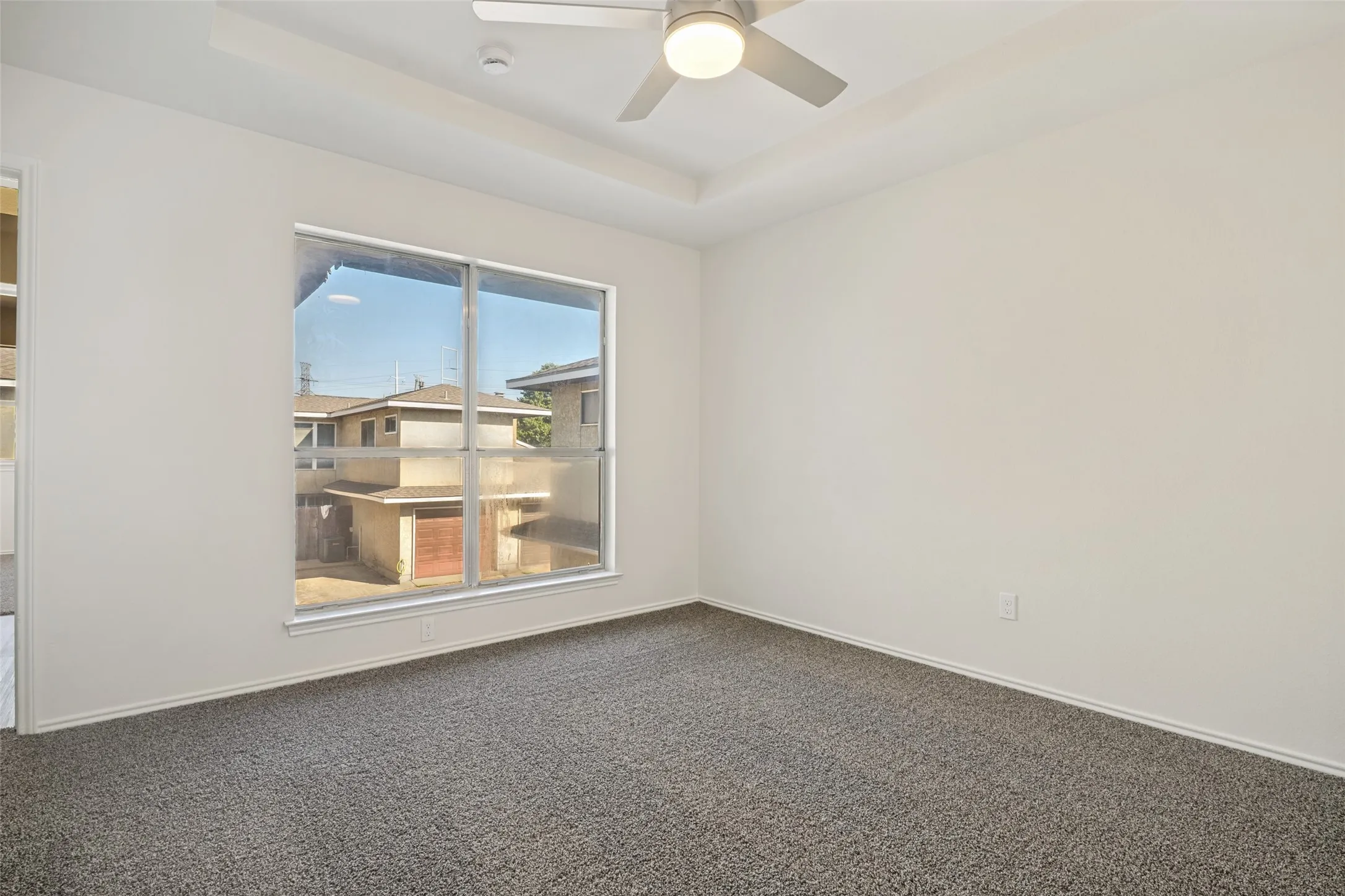 Room featuring neutral wall tones, gray carpeting, a tray ceiling, and an overhead ceiling fan with integrated lighting